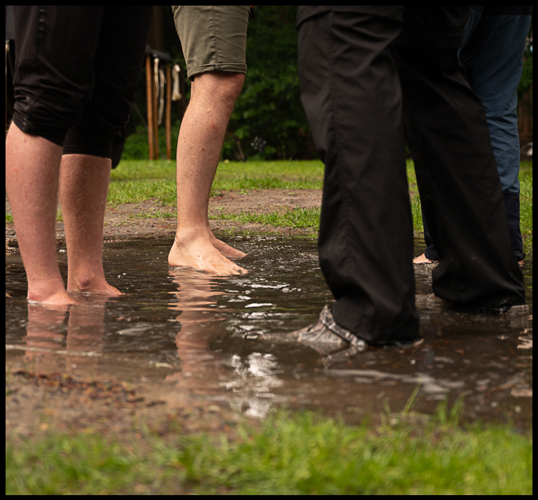 Mensen die hun voeten in een plas water steken in een groene buitenomgeving.