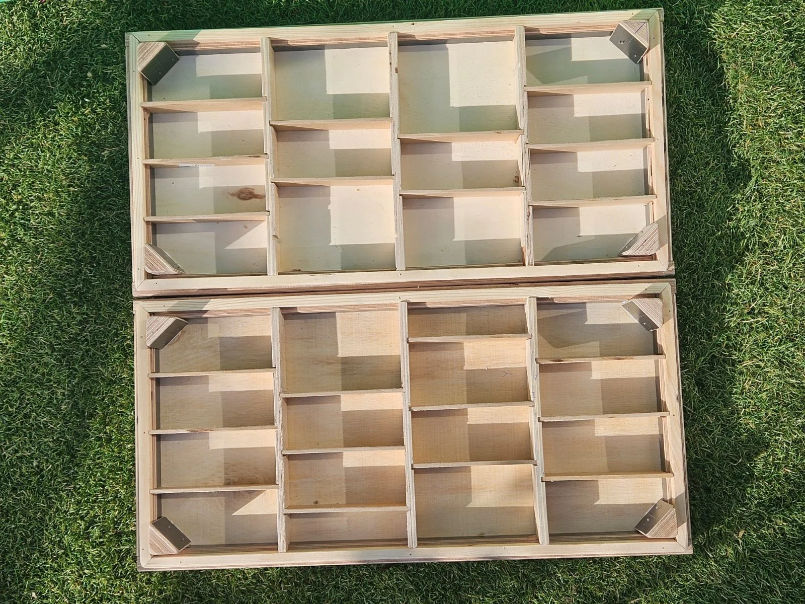Twee houten dienbladen met meerdere vakken, geplaatst op gras. Iedereen heeft vier metalen hoeken in elke hoek.