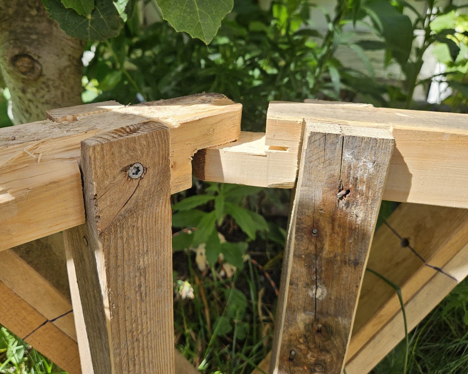 Close-up of a wooden pallet with some slats missing, outdoors with green foliage in the background.