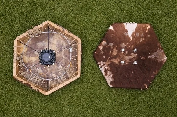 Disassembled hexagonal shade with a cowhide piece, placed on grass.