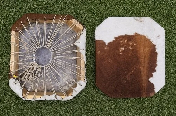 A cowhide rug and a saddle pad, both placed on grass.