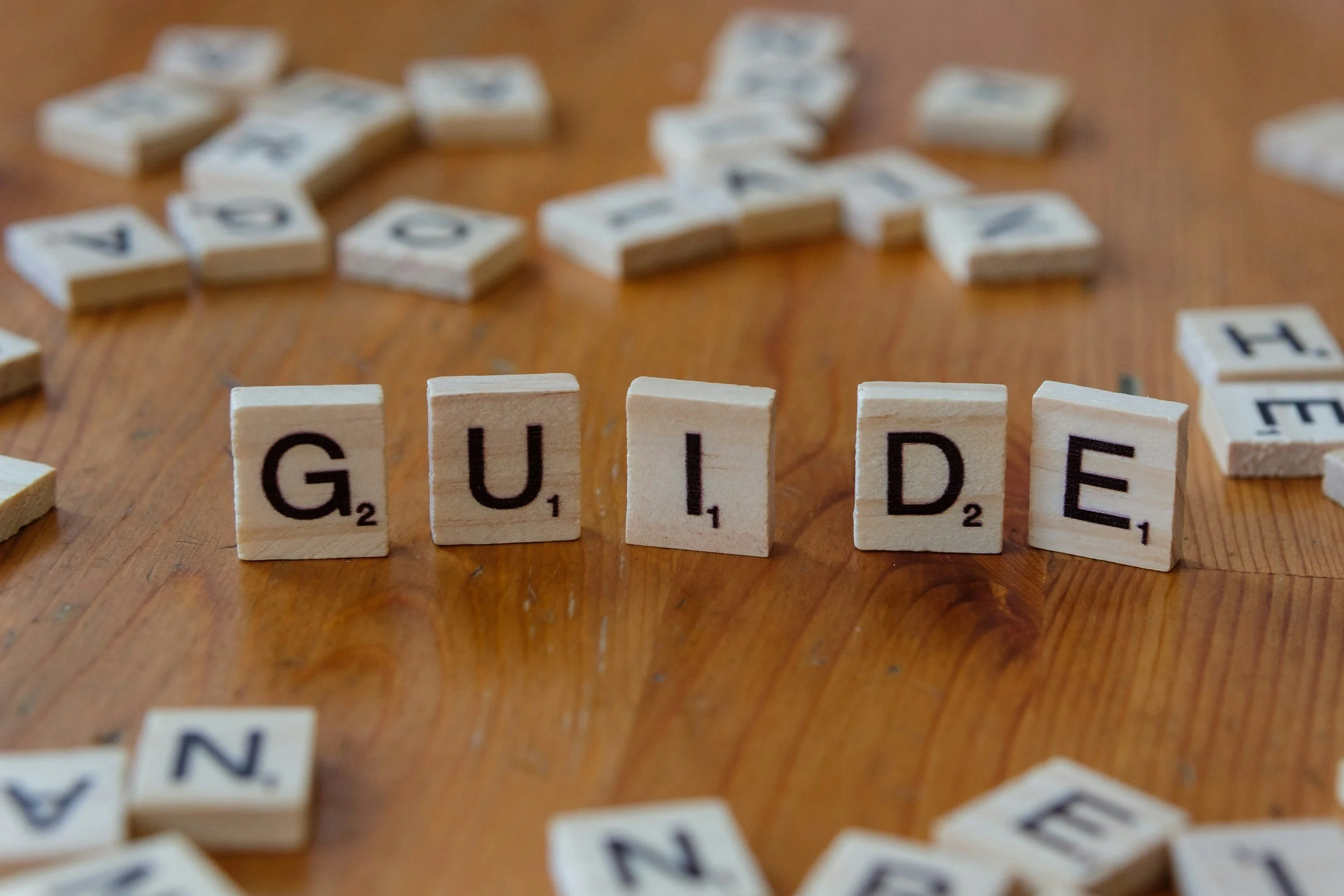 Scrabble tiles spelling out 'GUIDE' on a wooden surface.