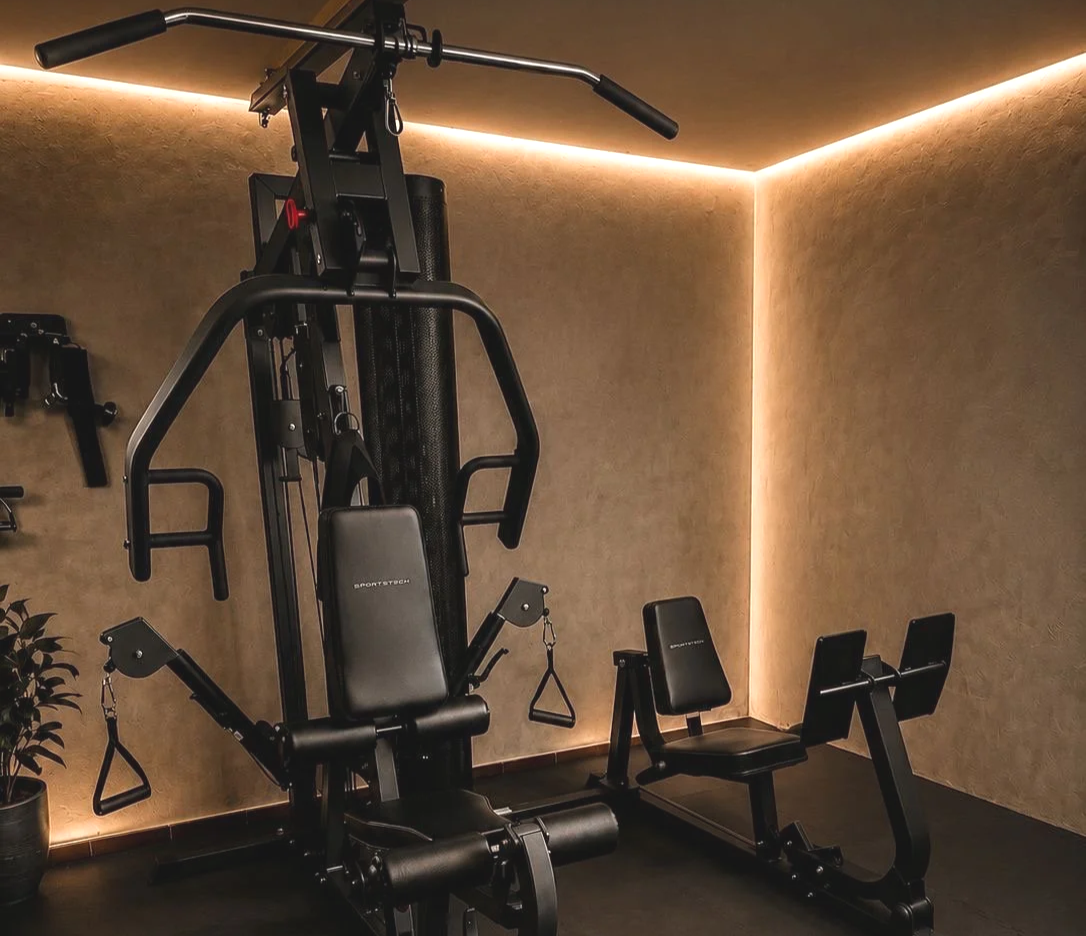 Fitnessgerät in einem Heimfitnessraum, beige Wände mit indirekter Beleuchtung, Pflanze in Topf.
