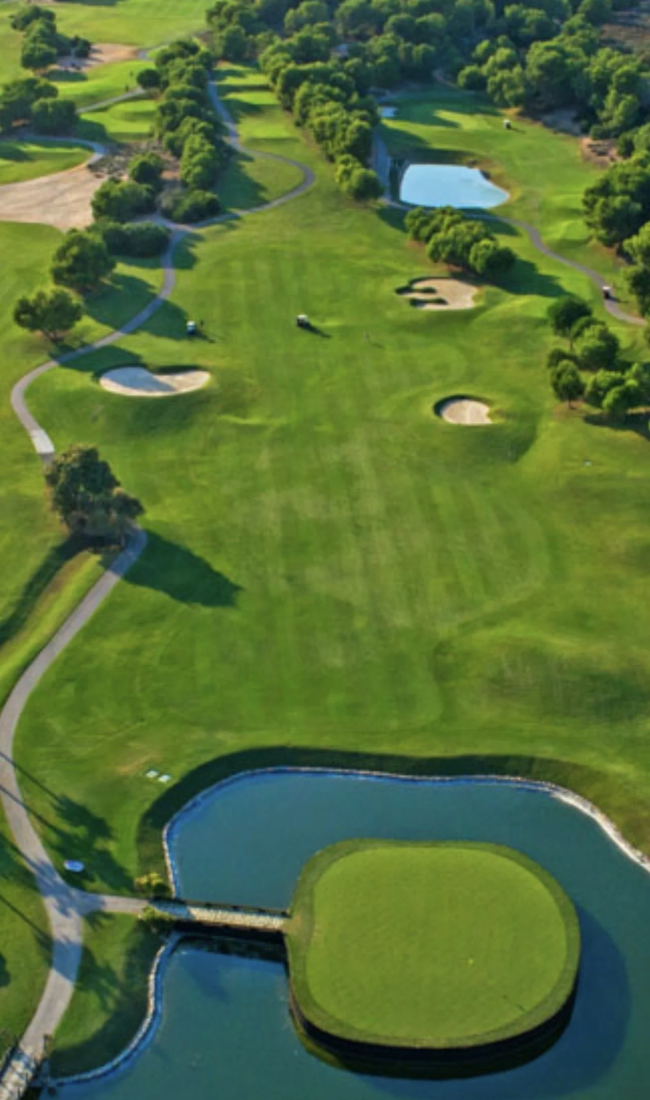 Aerial view of a golf course with green fairways, sand traps, water hazards, and trees lining the course.