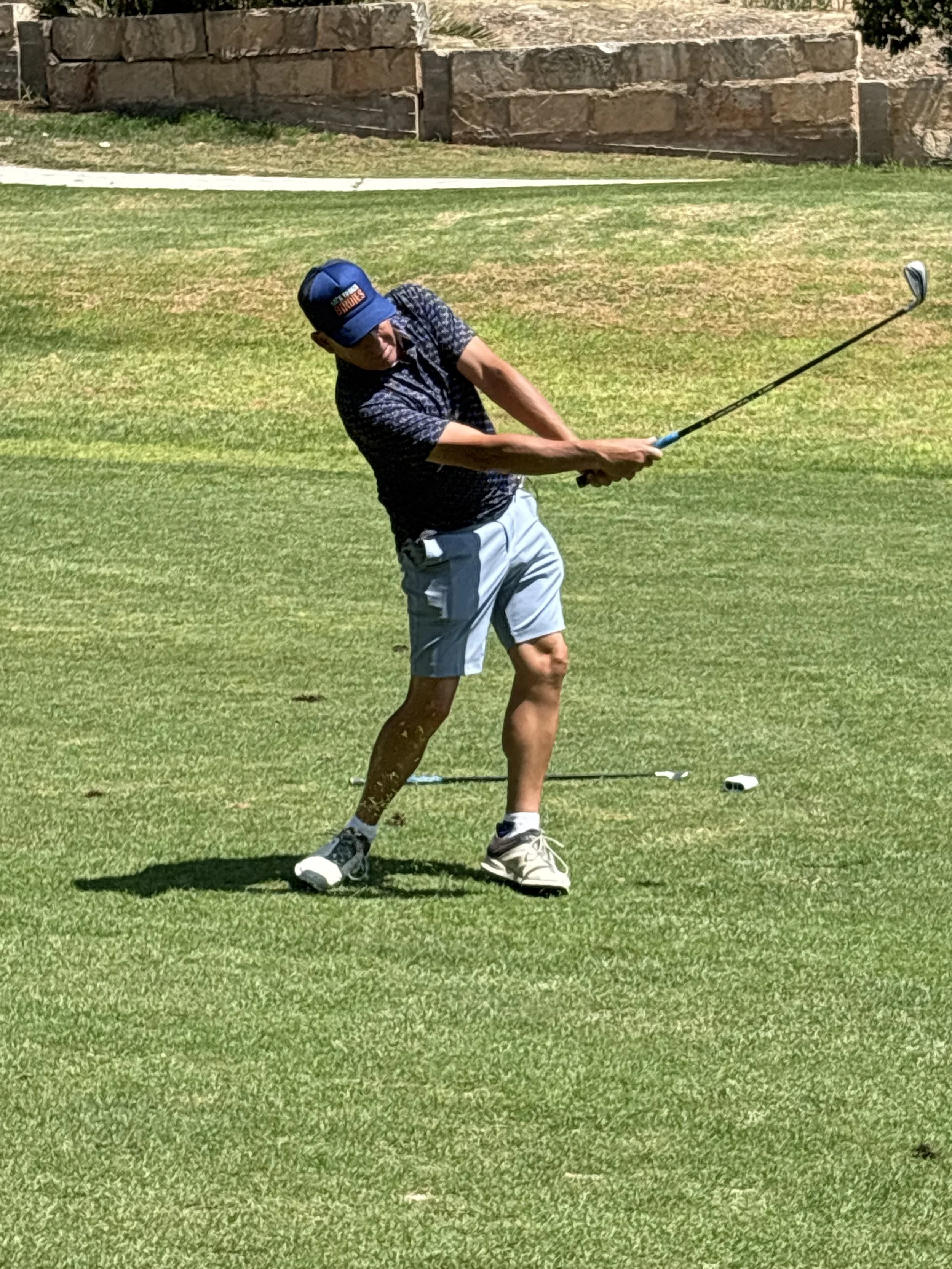 A man playing golf indoors on a green mat, swinging a golf club.