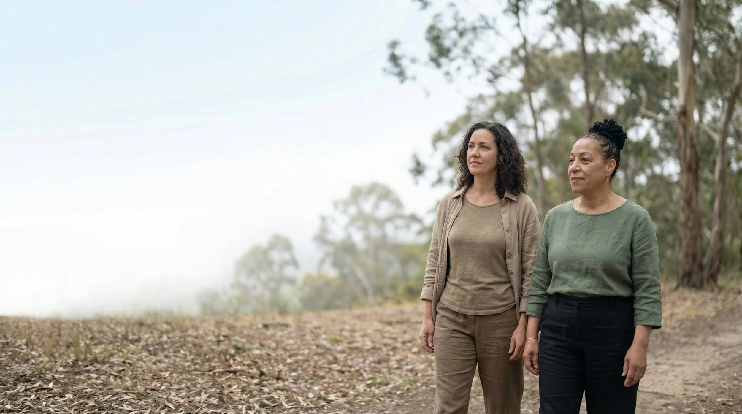 Two women walking outdoors in a field with trees in the background.