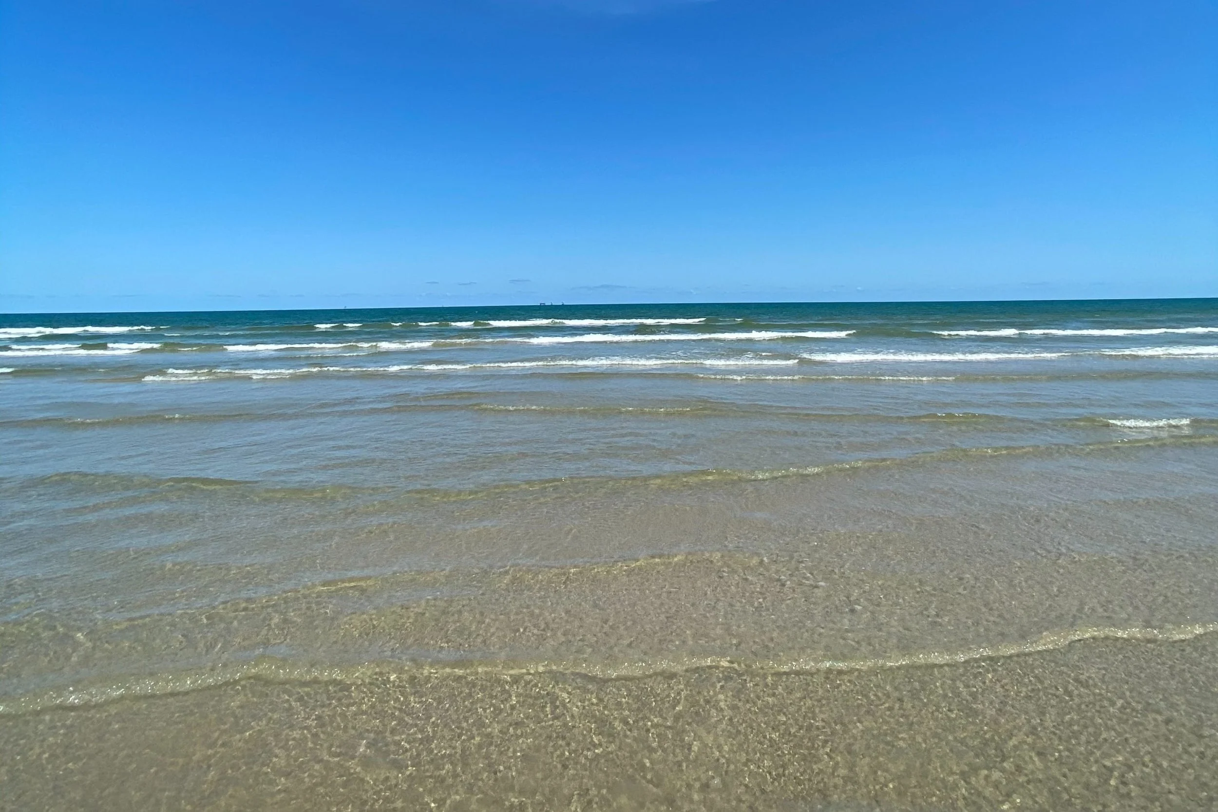 Calm ocean waves gently hitting the sandy beach under a clear blue sky.