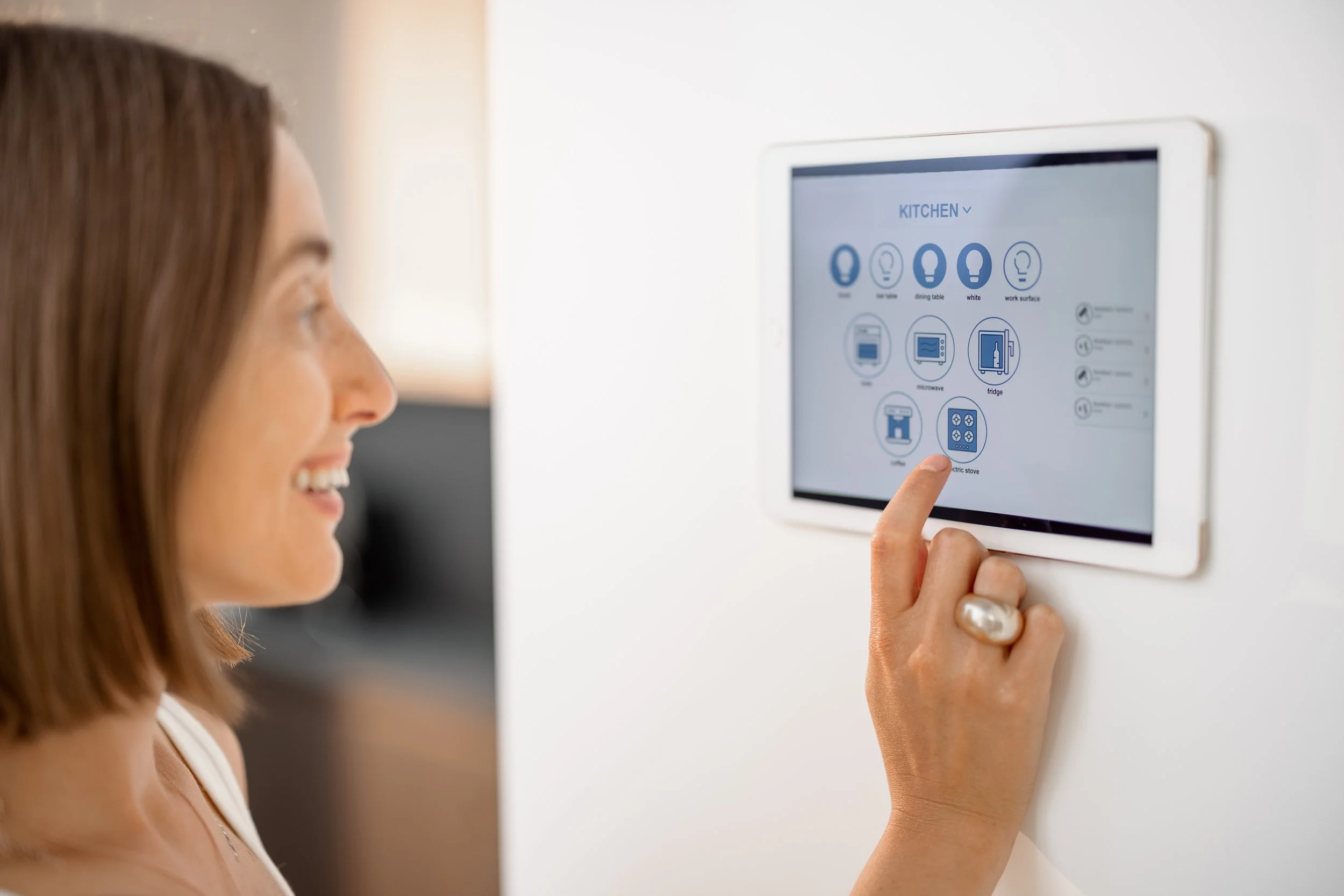Woman interacting with a wall-mounted smart home control panel with icons for lighting, appliances, and settings.