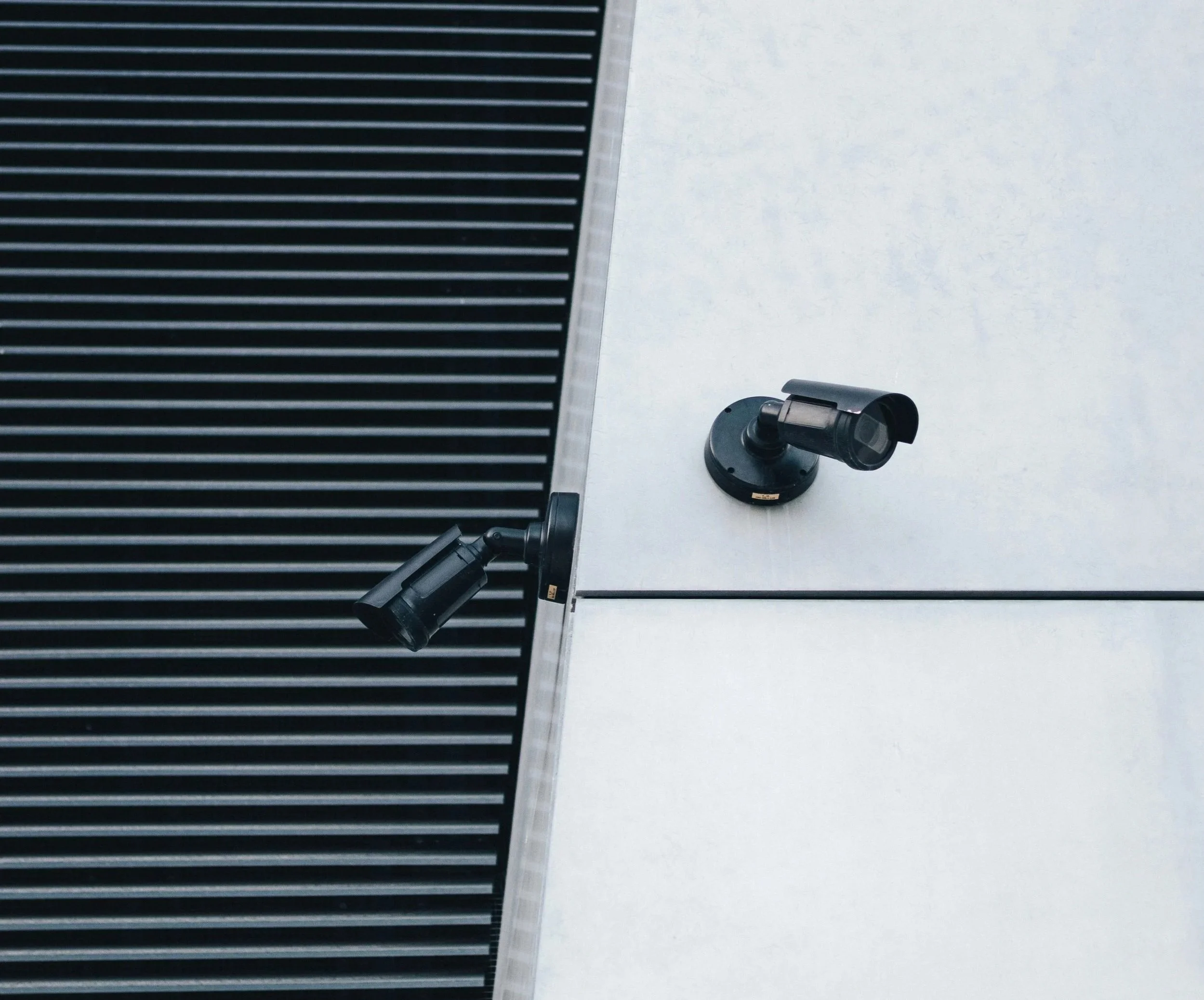 Two security cameras placed on different parts of a building exterior, one pointed to the left and the other to the right, with a black and white building facade.