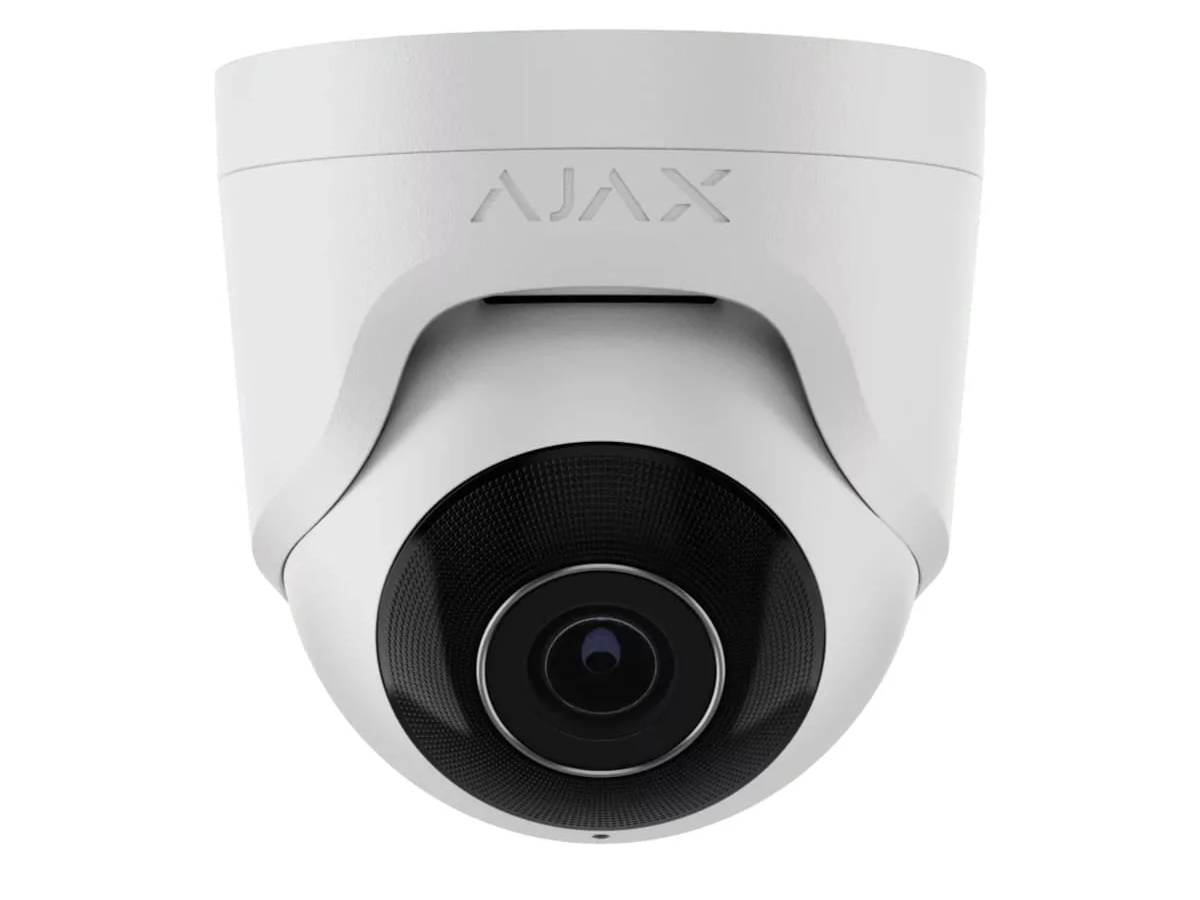 A white security camera with a black circular lens, mounted on a white surface.