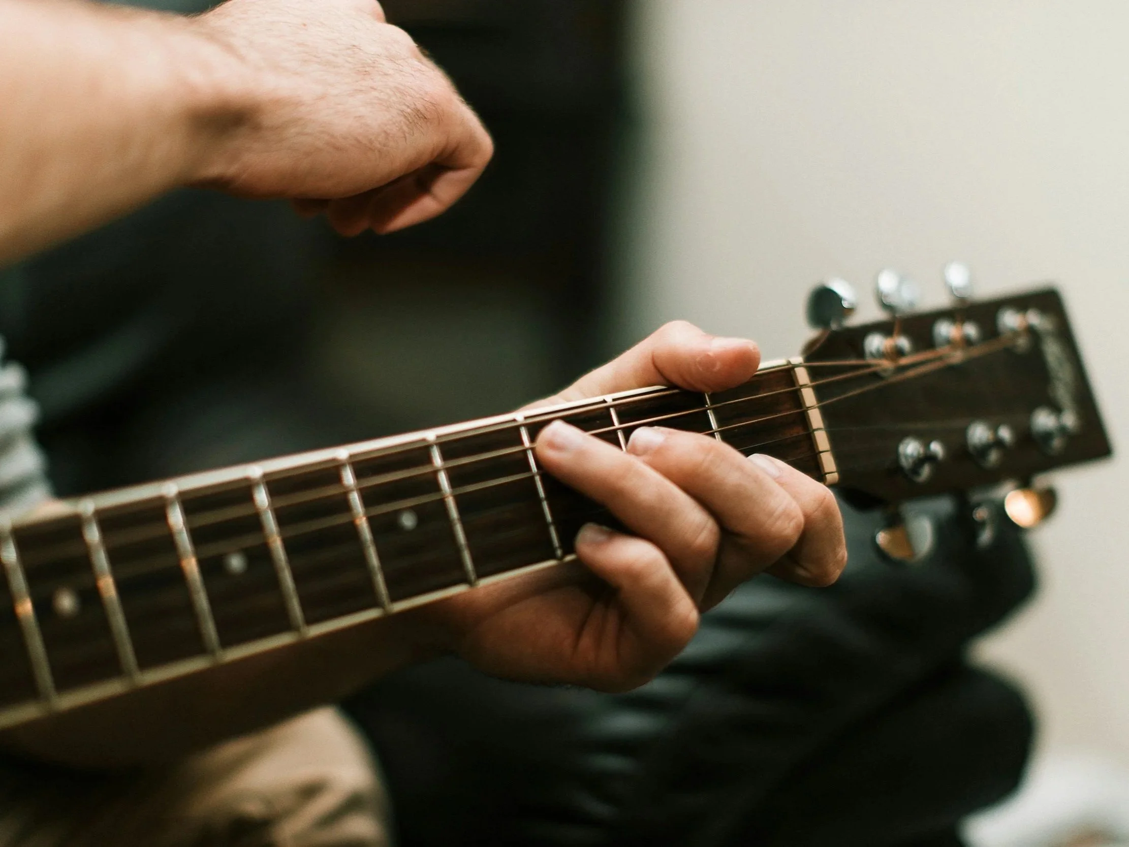 Close-up of a person playing an acoustic guitar, focusing on their hand on the fretboard.