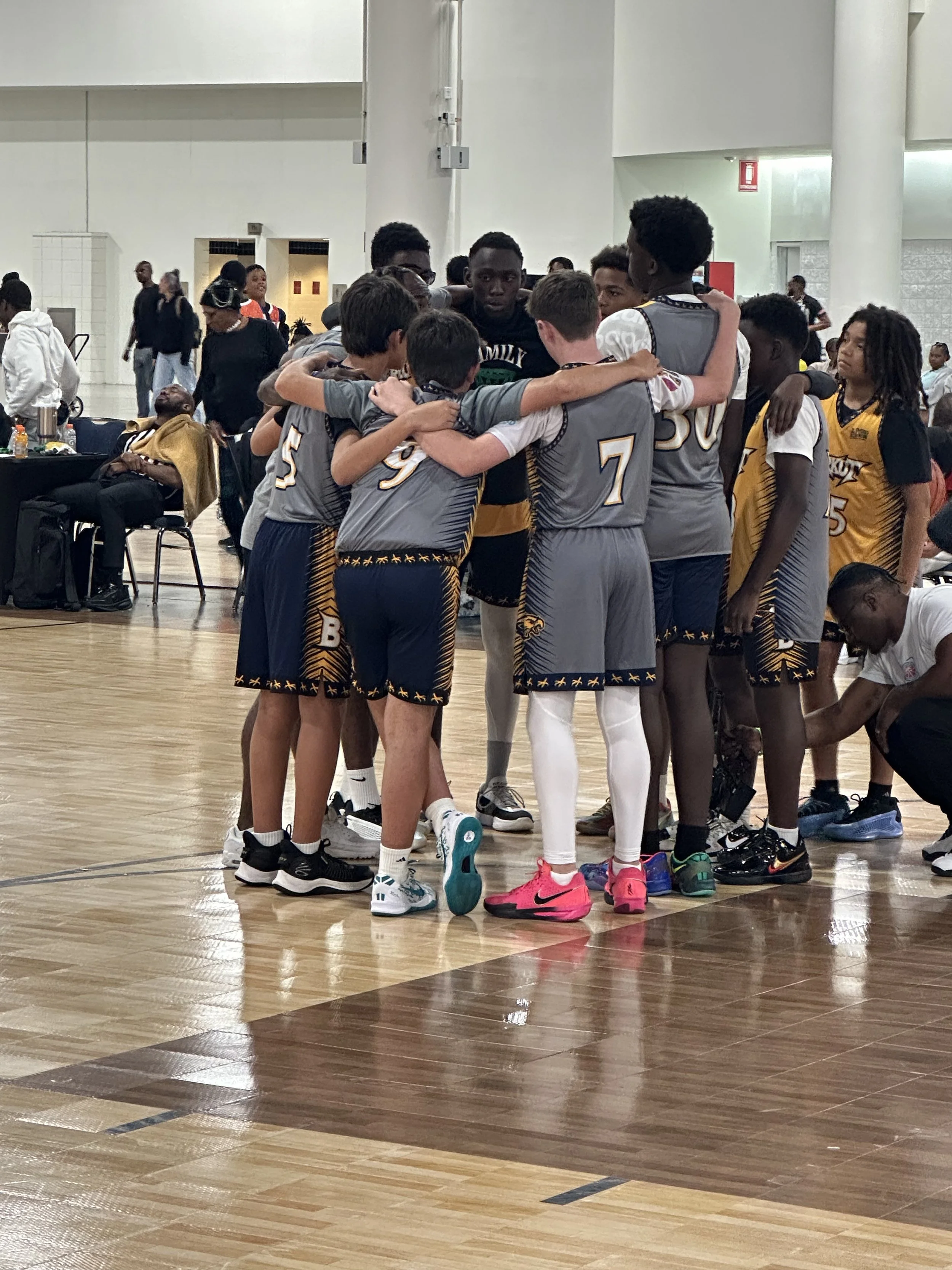 A group of young basketball players in cheerleading huddle on an indoor court.