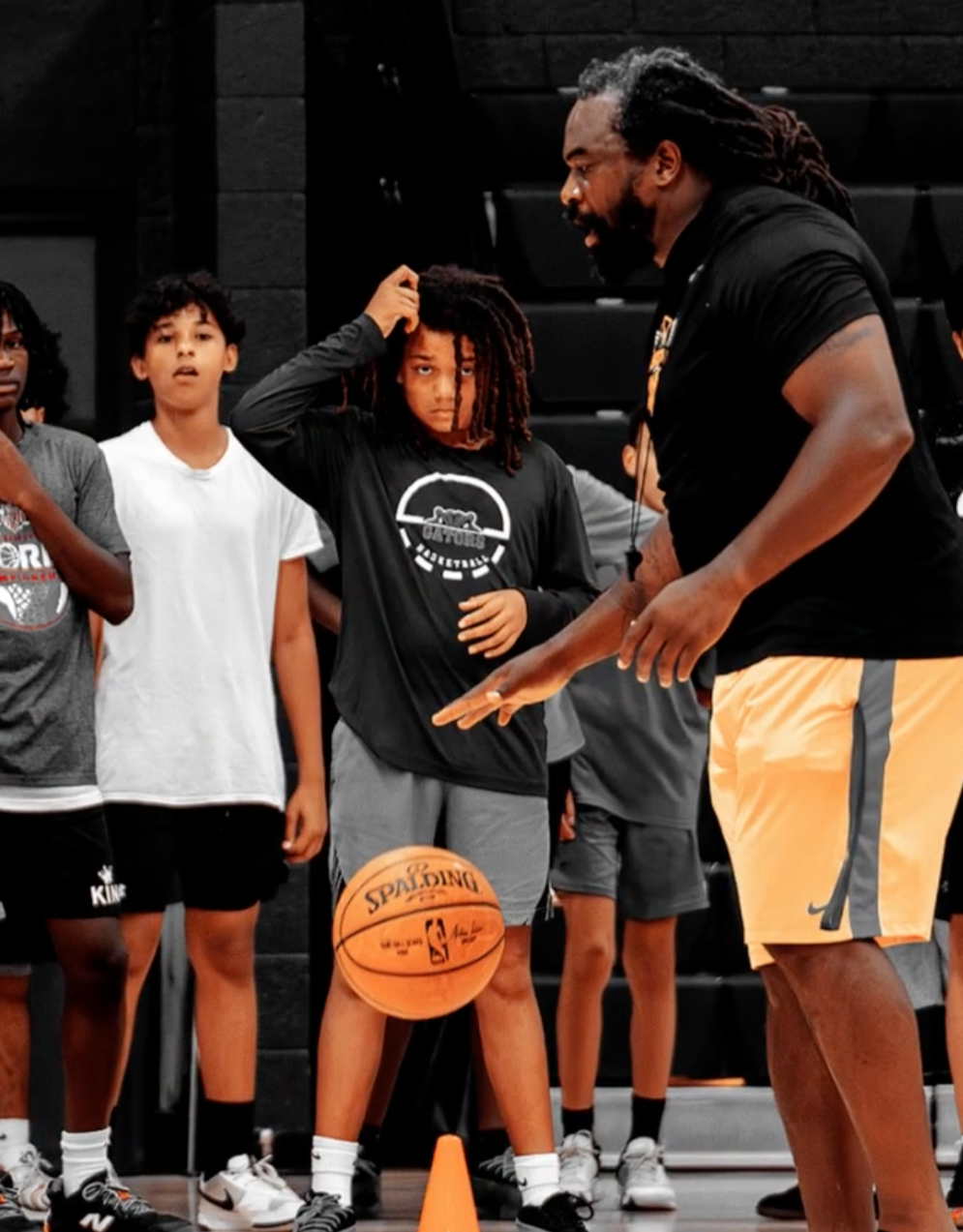 Basketball coach instructing young players during practice in an indoor gym.