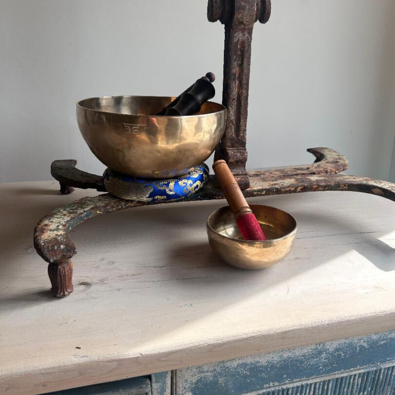 A sound worshop set up with brass tibetan singing bowls, and a crystal pendulum on a vintage wooden table.