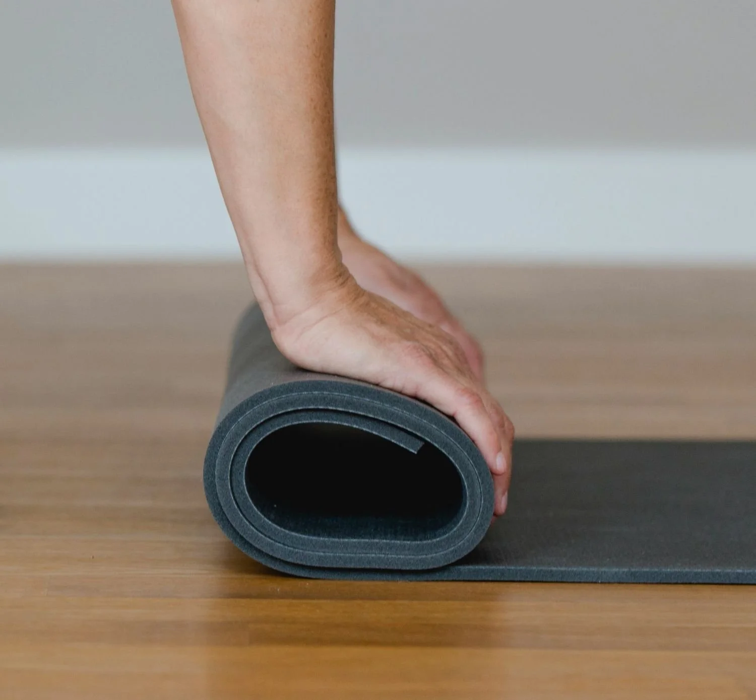Person rolling out a yoga mat on a wooden floor.