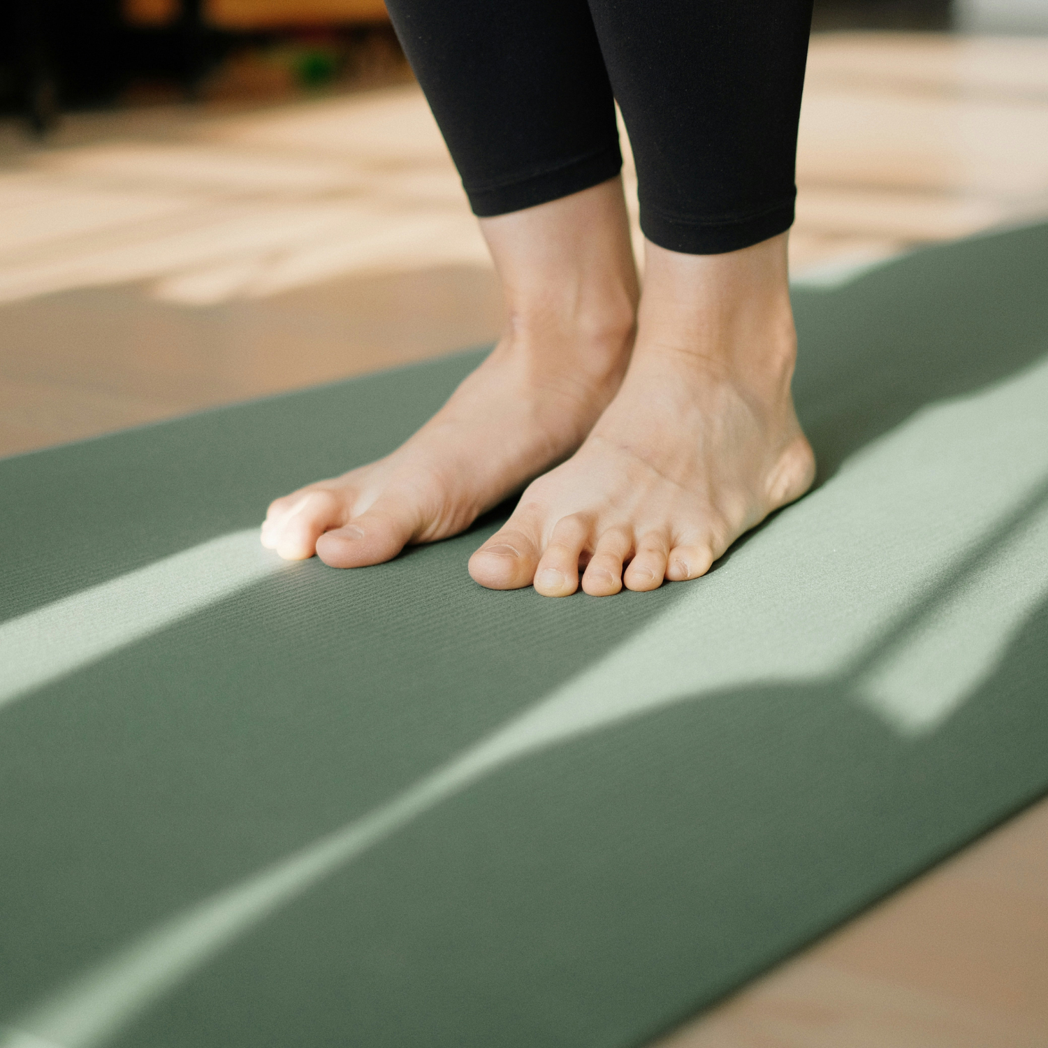 Person standing on a green yoga mat, wearing black leggings, in a yoga studio.