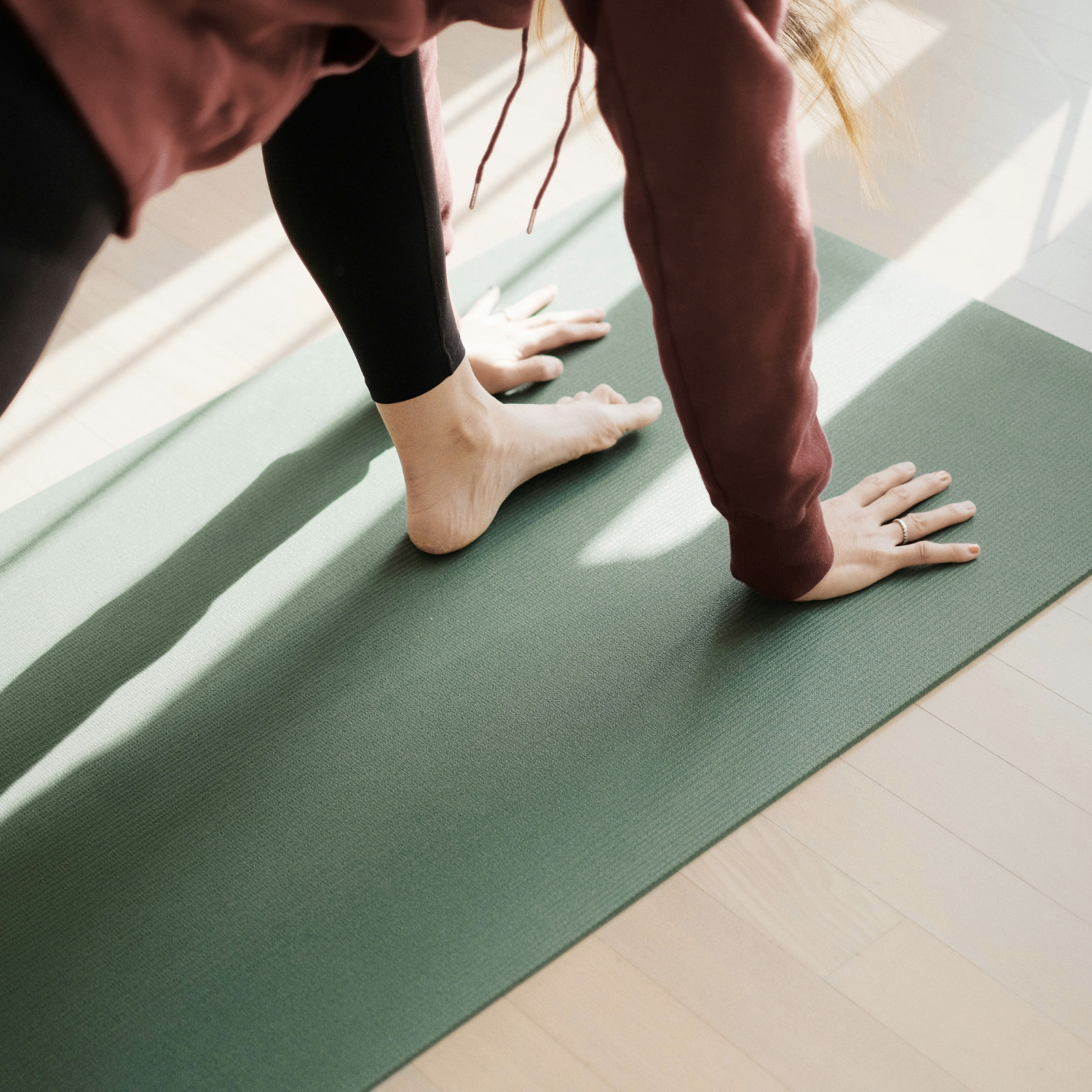 Person practicing yoga on a green mat with hands and feet on the ground, wearing black leggings and a red long-sleeve top.