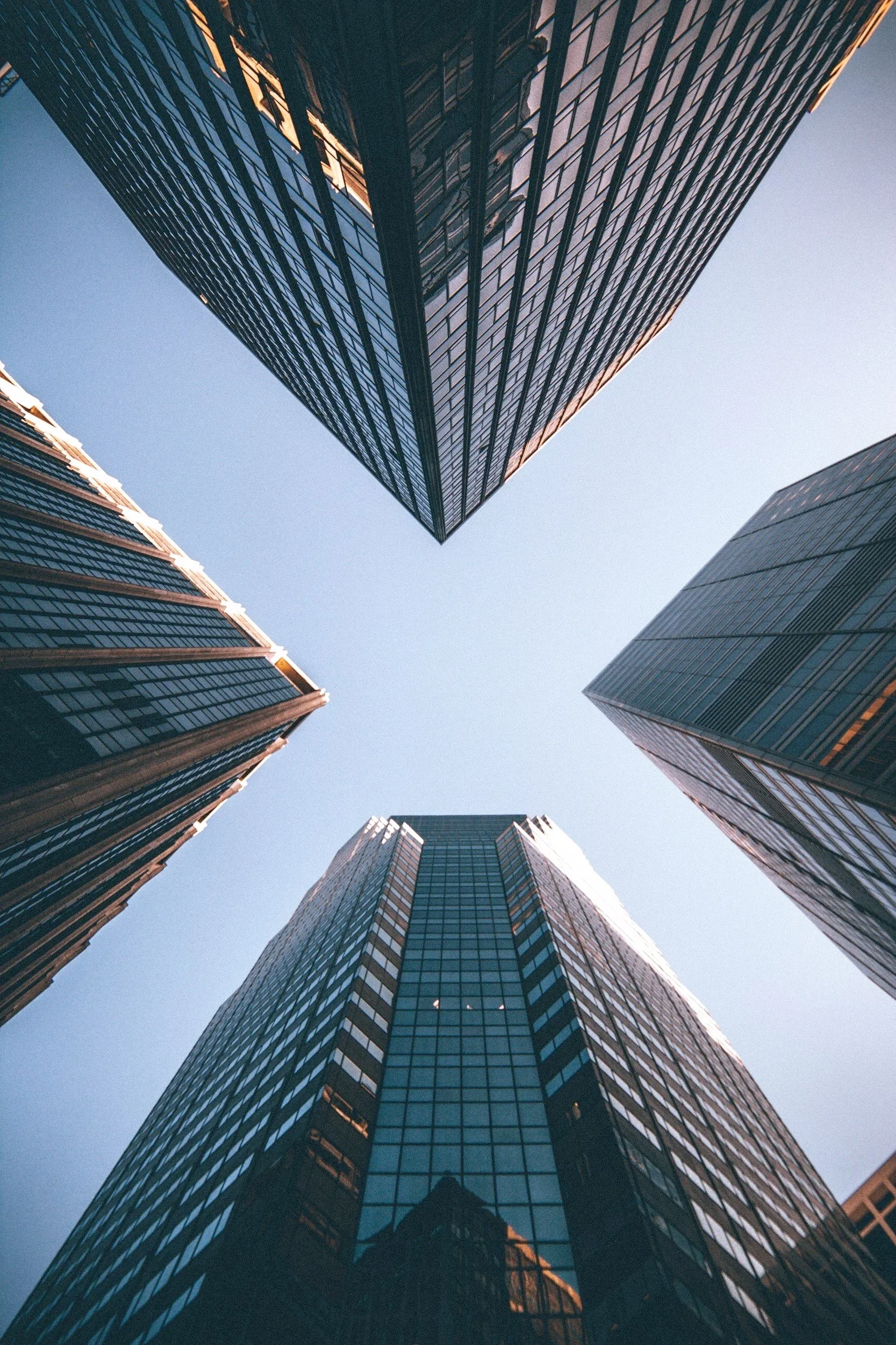 Looking up at four tall modern glass skyscrapers in a city.