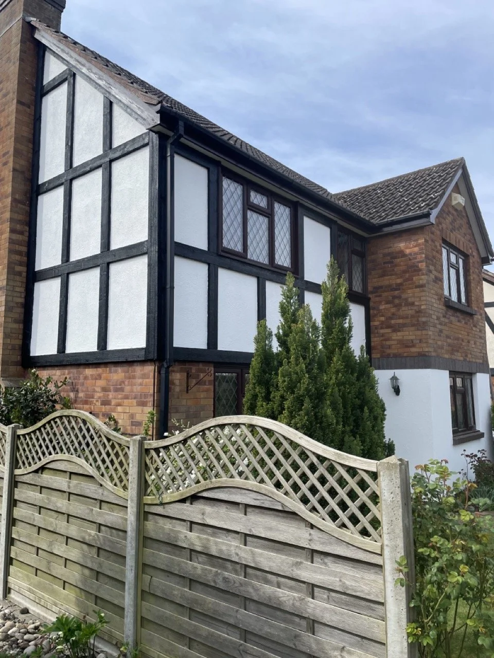 Exterior residential house with black wood panel freshly painted and fresh white walls surrounded by shrubbery and a weaving pattern wooden fence