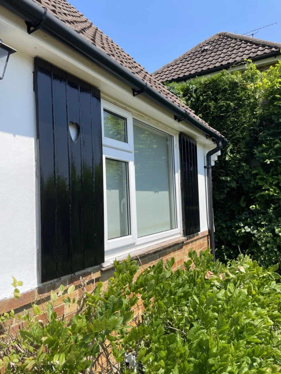 Country house shutters freshly painted in black gloss paint on a white house surrounded by shrubbery