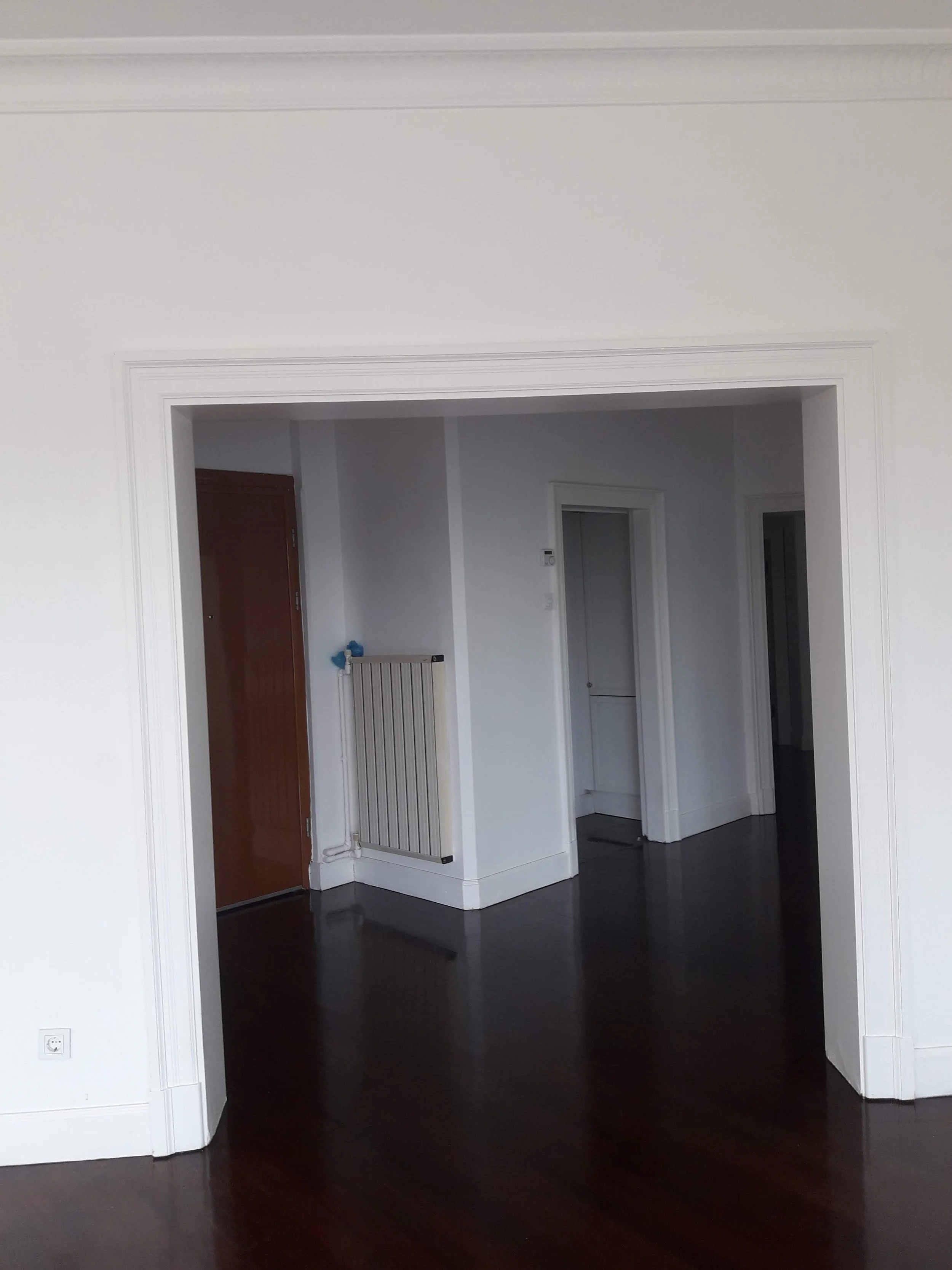 Empty room with dark wooden floors, white walls, and doorways leading to other rooms.