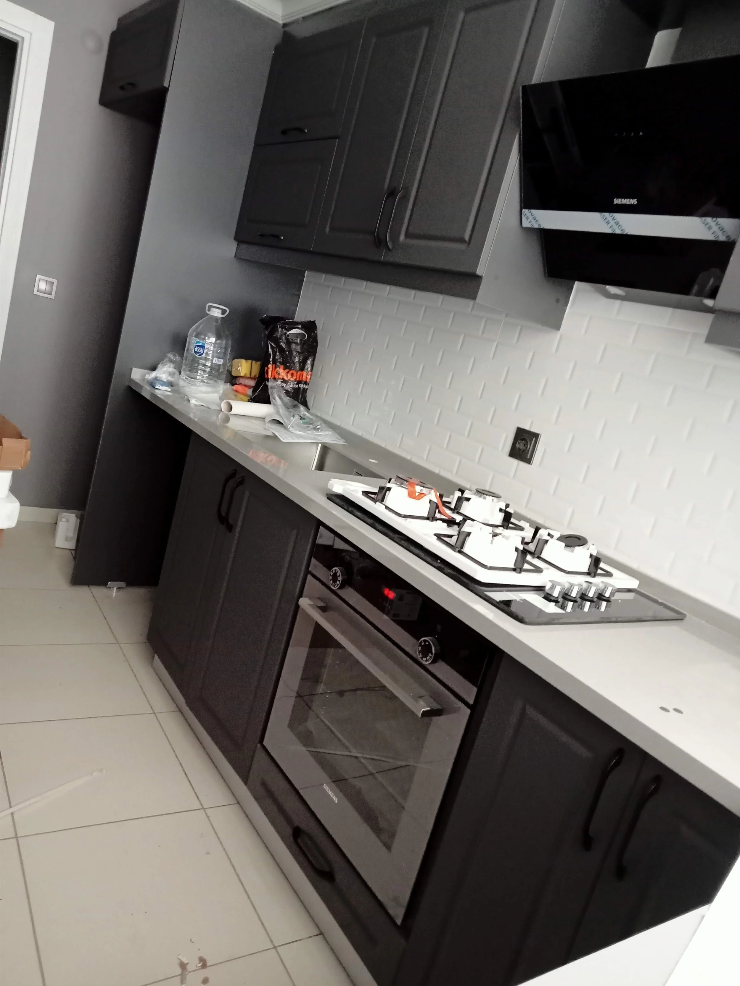 Kitchen with black cabinets, a gas stove, a modern oven, a black microwave, and a white tiled backsplash.