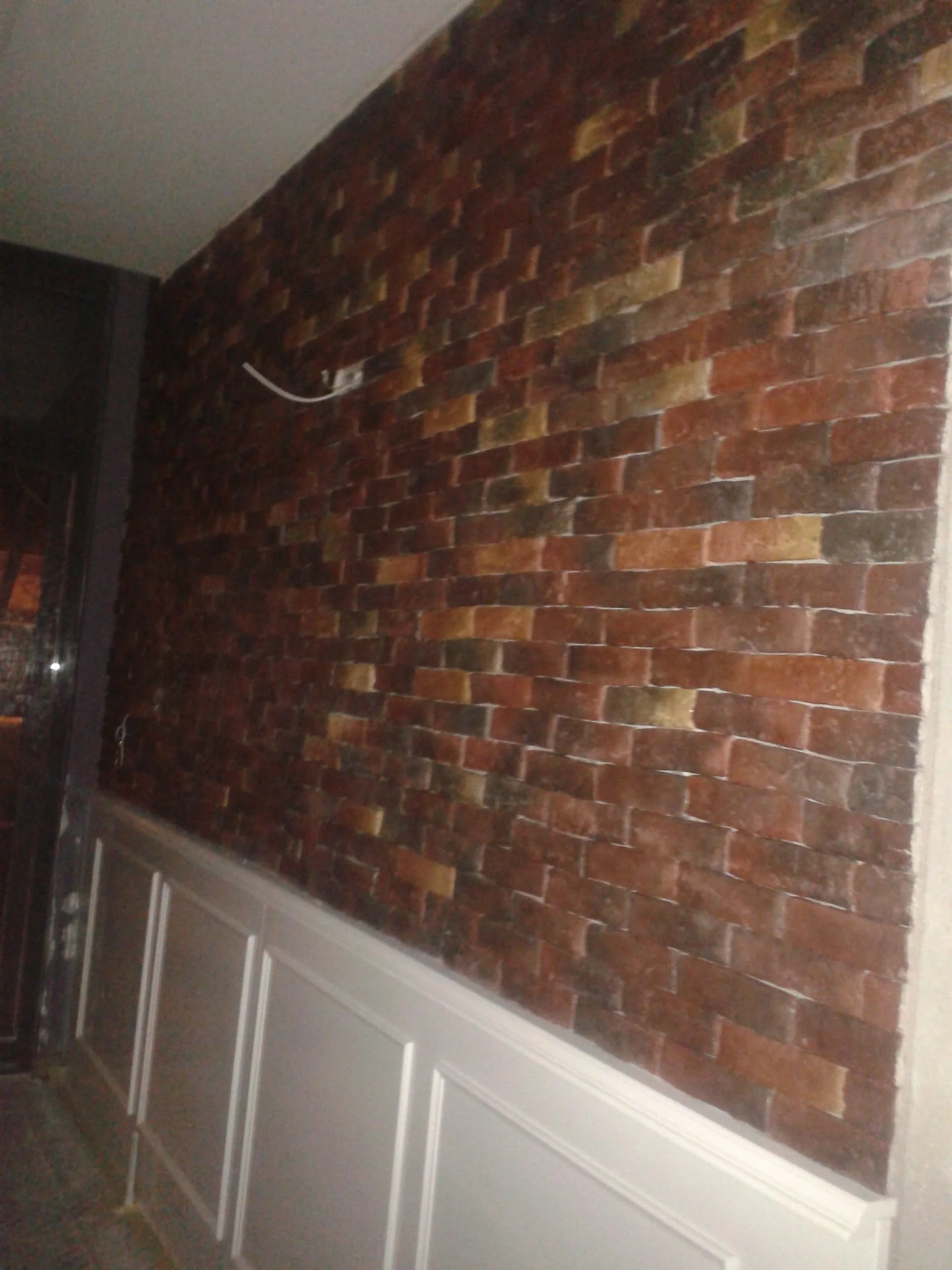 Interior room with exposed red brick wall above white wainscoting, electrical wires hanging from the wall.