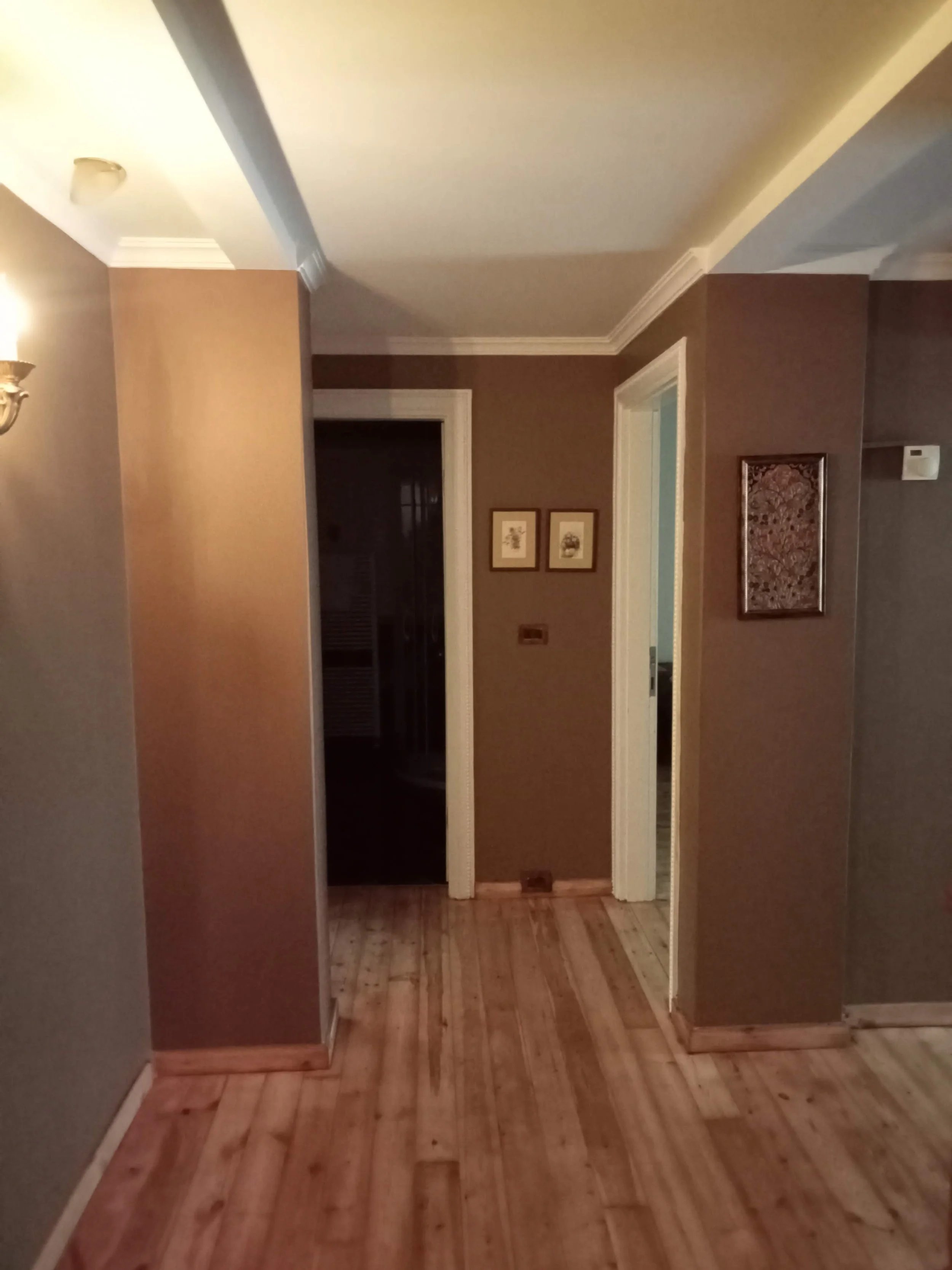 Interior of a home with a hallway, brown walls, wooden floor, and framed artwork.