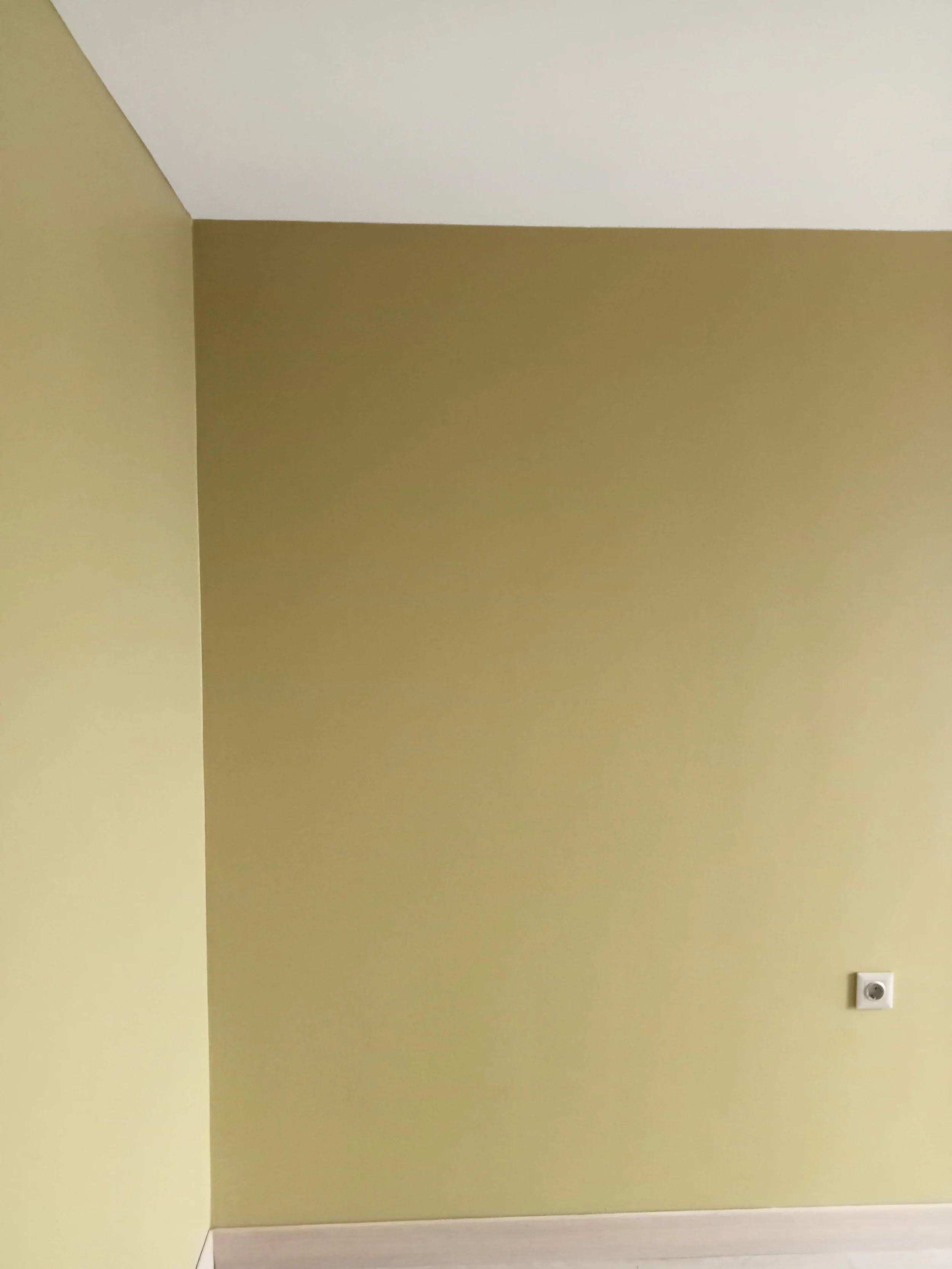 Empty room with yellow walls, white ceiling, one electrical outlet on the right wall, and light-colored flooring.
