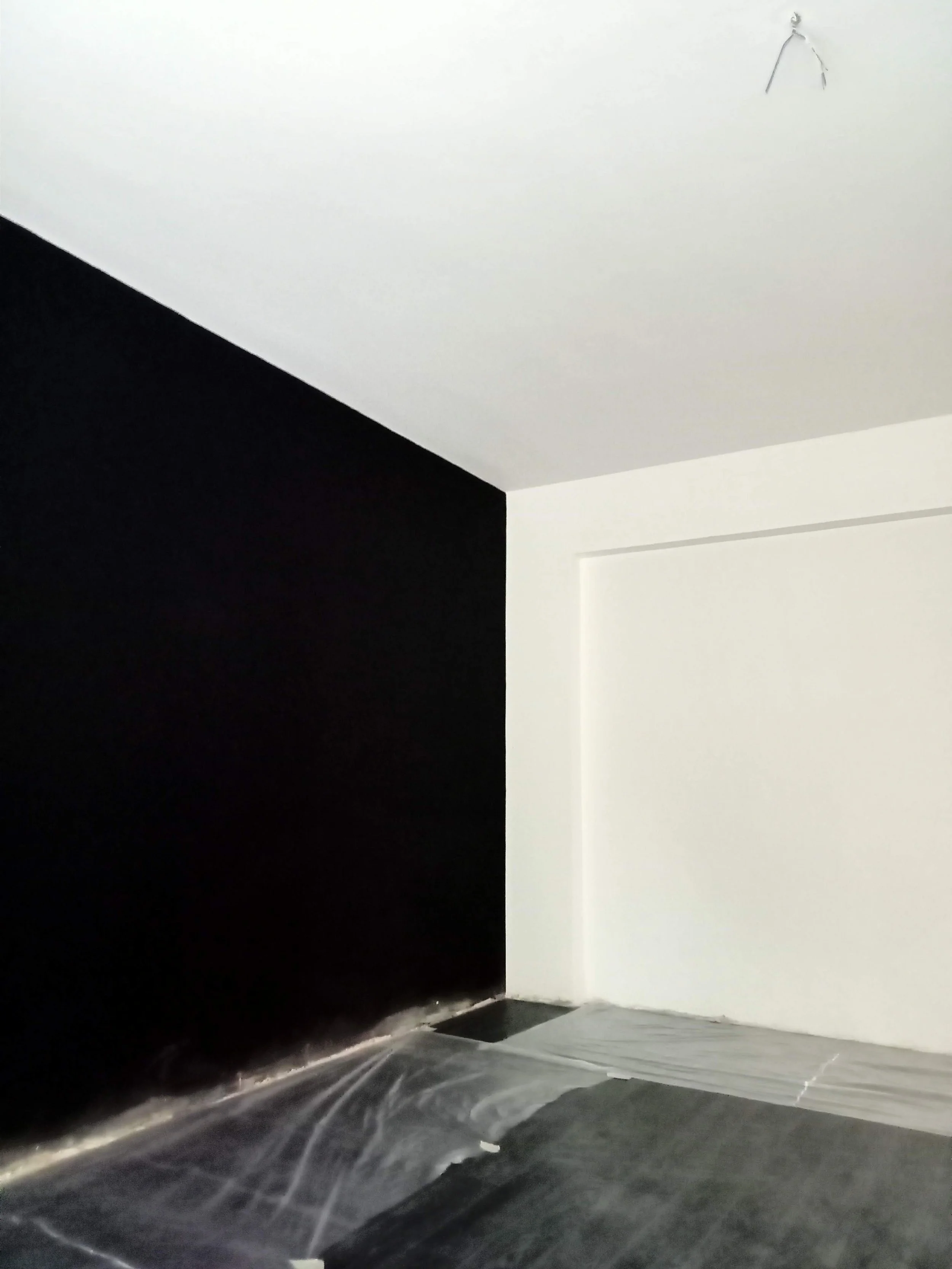 Corner of a room with black and white walls, and a covered floor, possibly under construction or renovation.