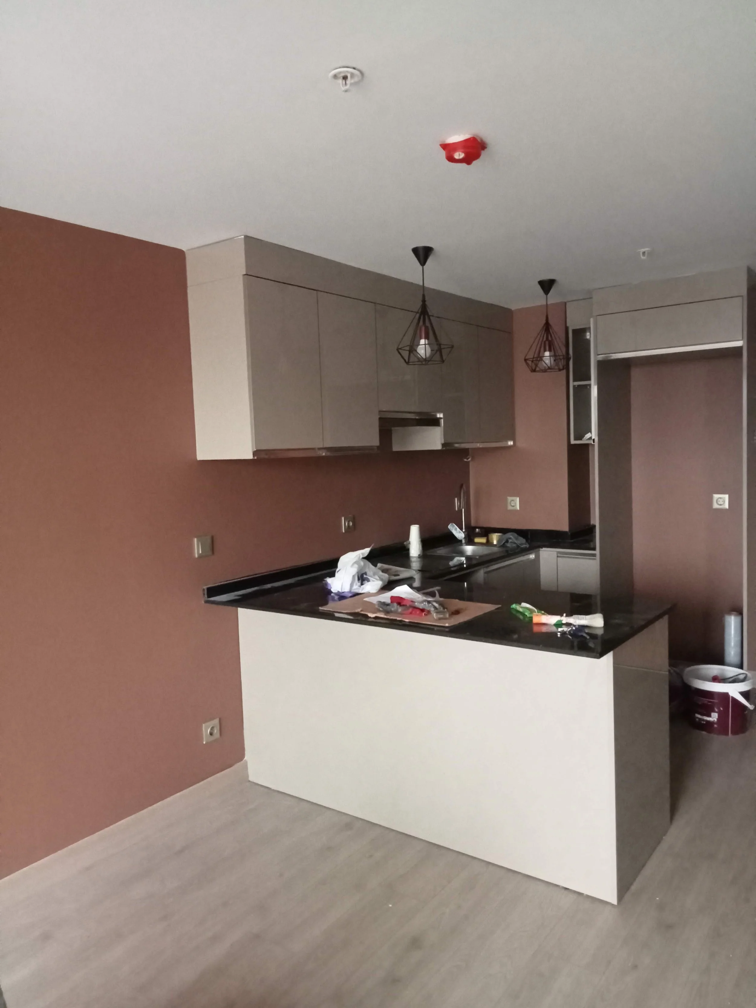 Unfinished modern kitchen with a black countertop, gray cabinets, and pendant lights, with cleaning supplies and debris on the counter.