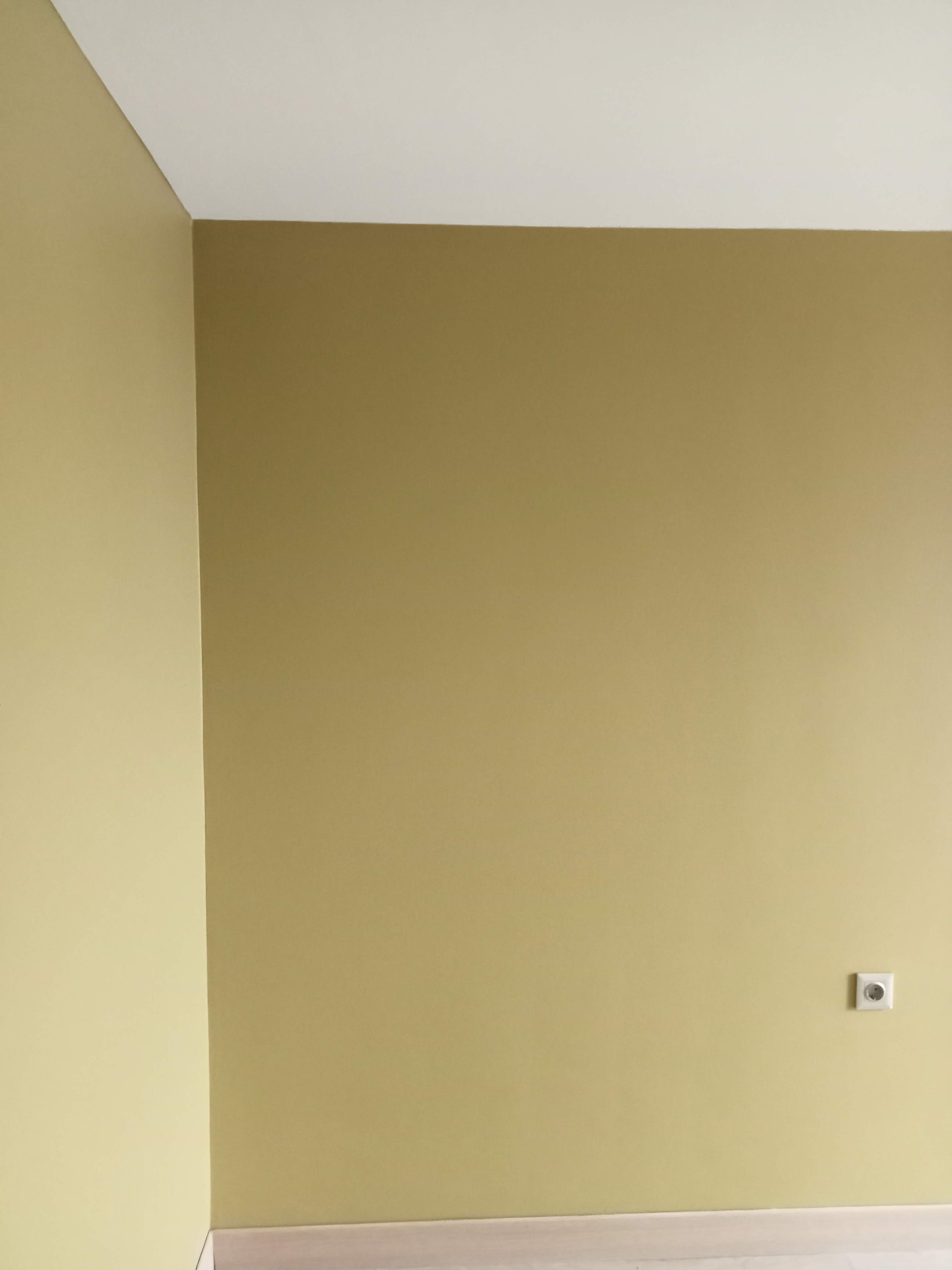 Empty room with yellow and beige walls and white ceiling showing a wall outlet near the floor.