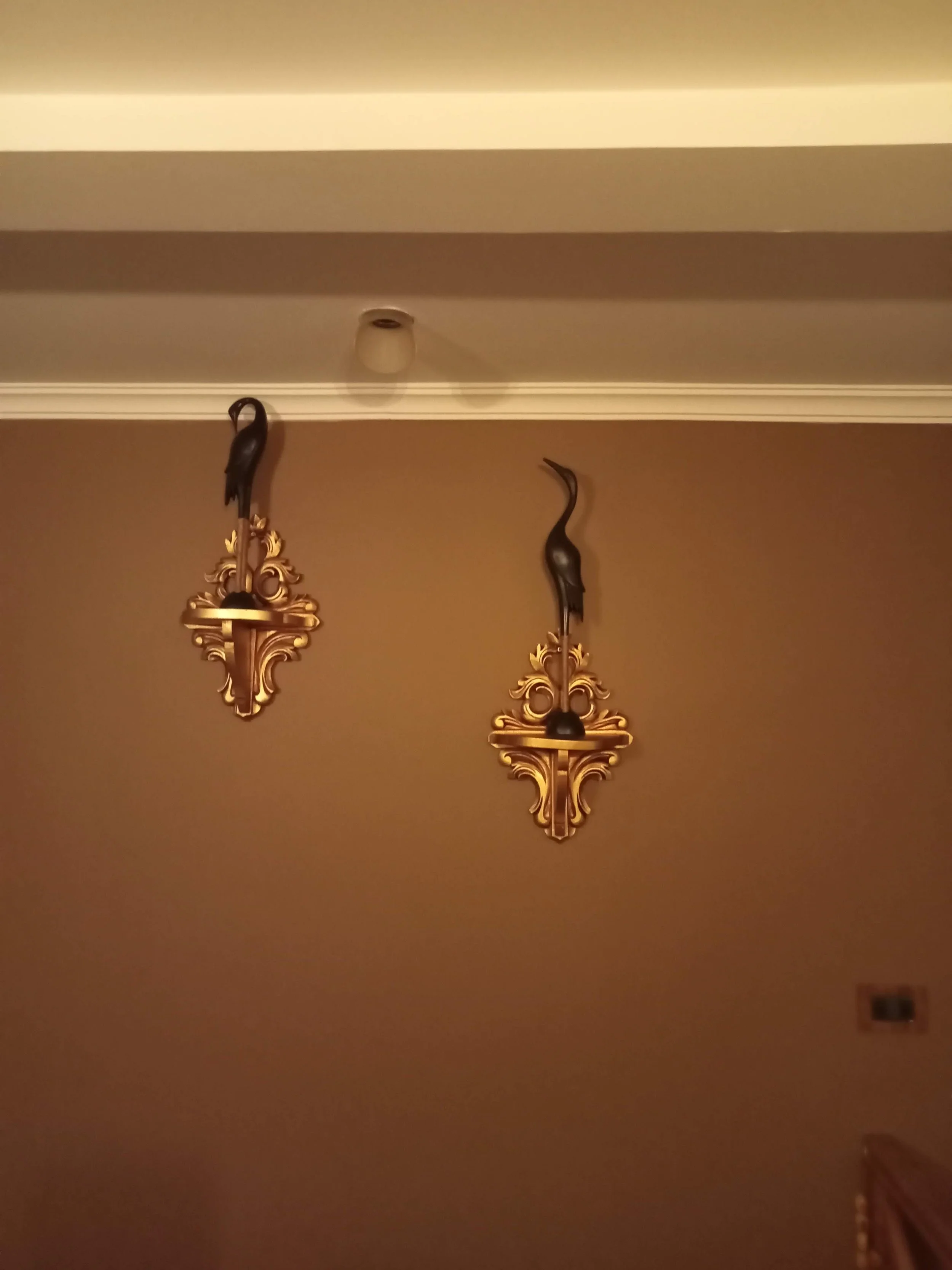 Two decorative wall sconces with bird sculptures on a beige wall.