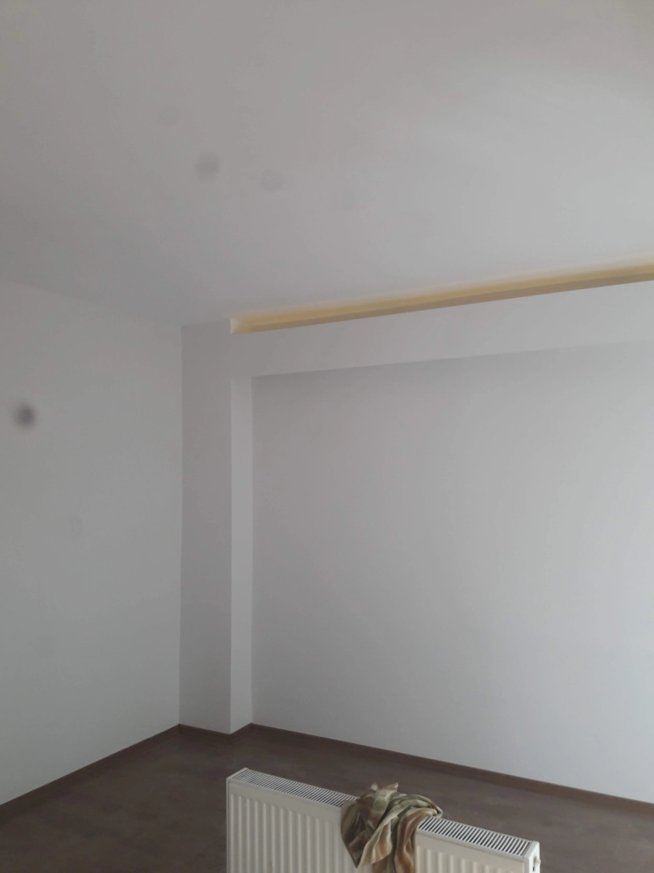 Empty white room with a radiator and a section of ceiling with a yellow trim, plain gray walls, and a hardwood floor