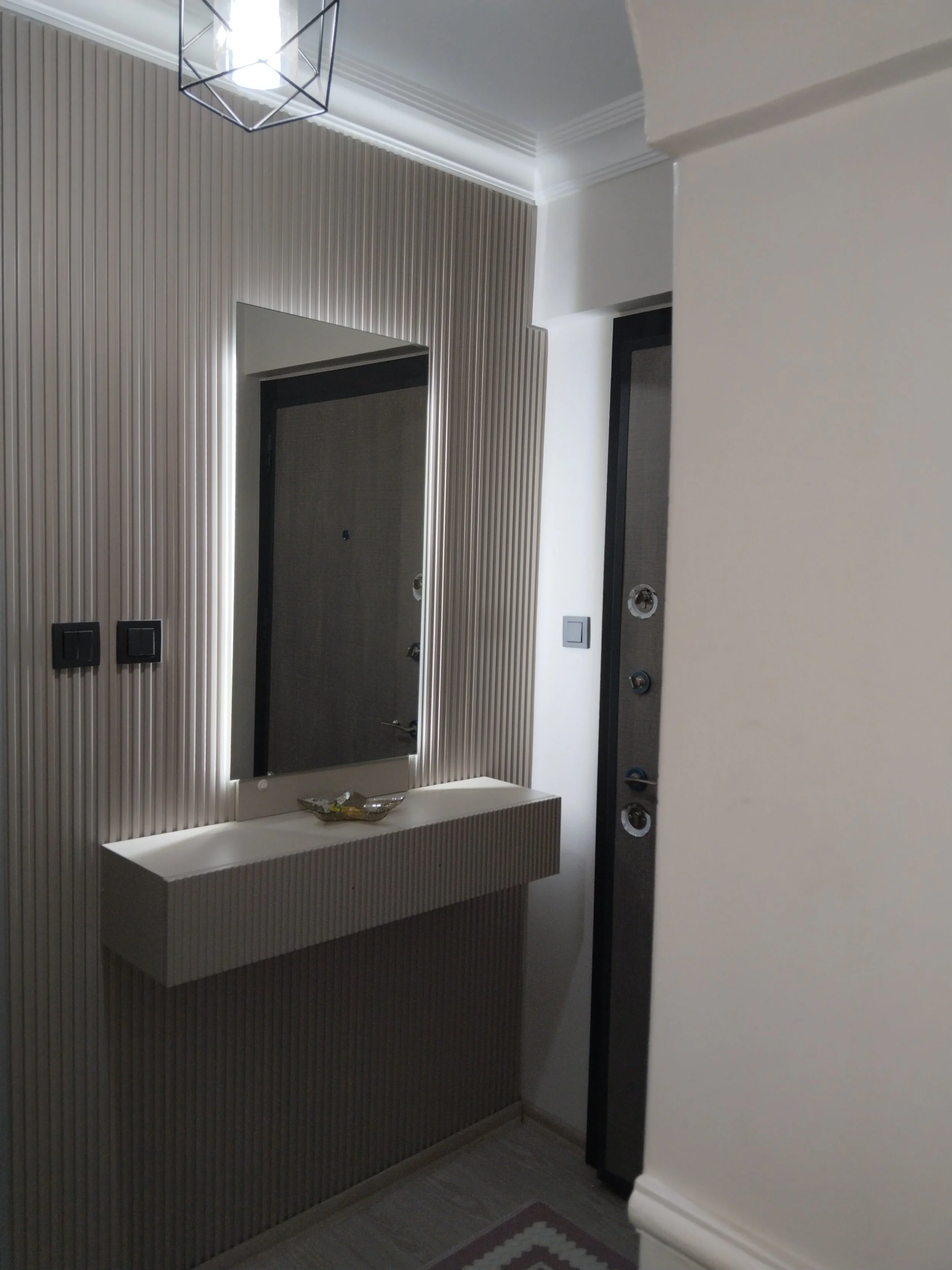 Modern entryway with a textured wall panel, a large mirror, a floating sink, and a door with exposed hardware.