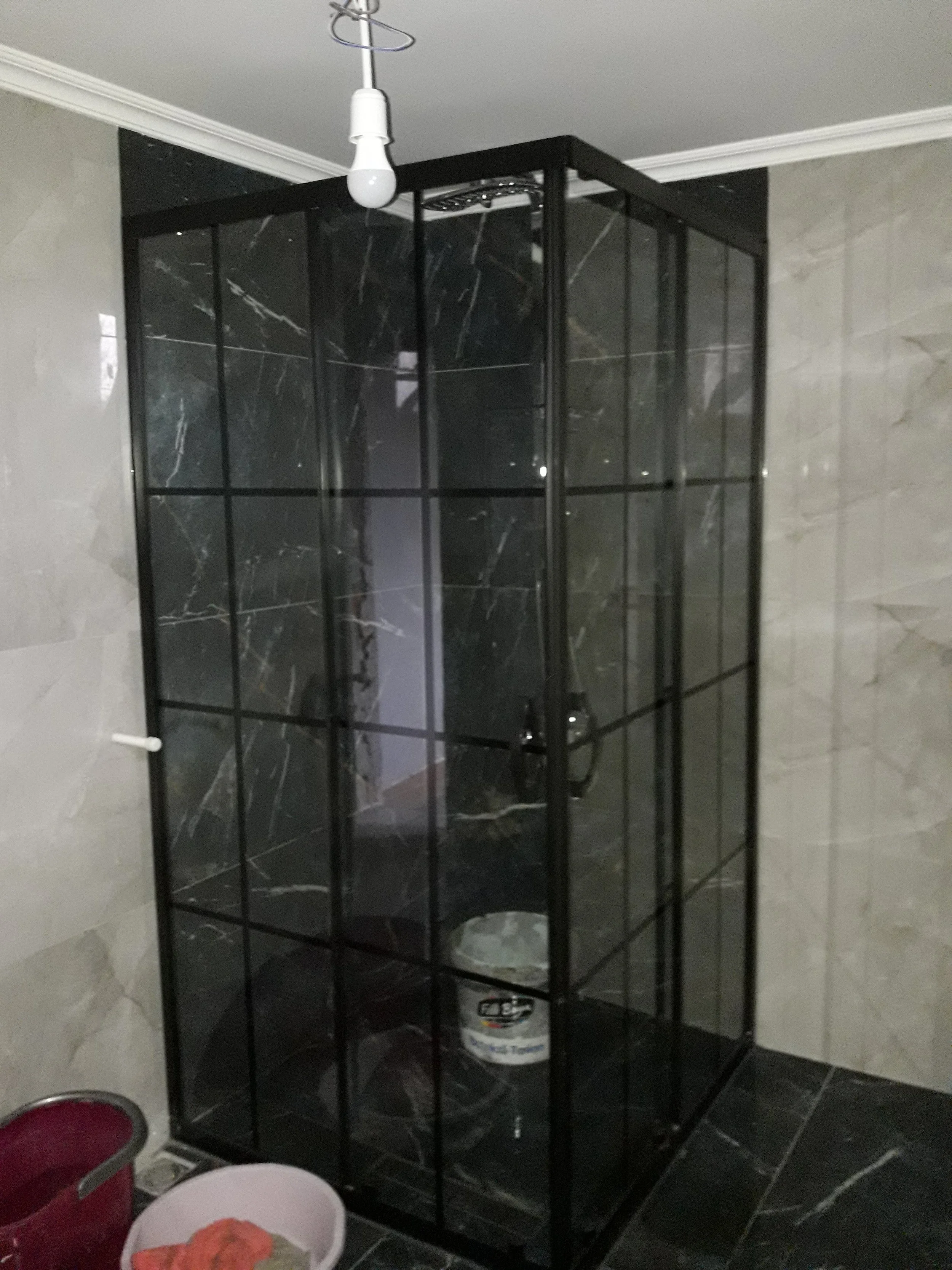 A shower stall with black marble walls and a glass door in a bathroom, containing a bucket on the floor.
