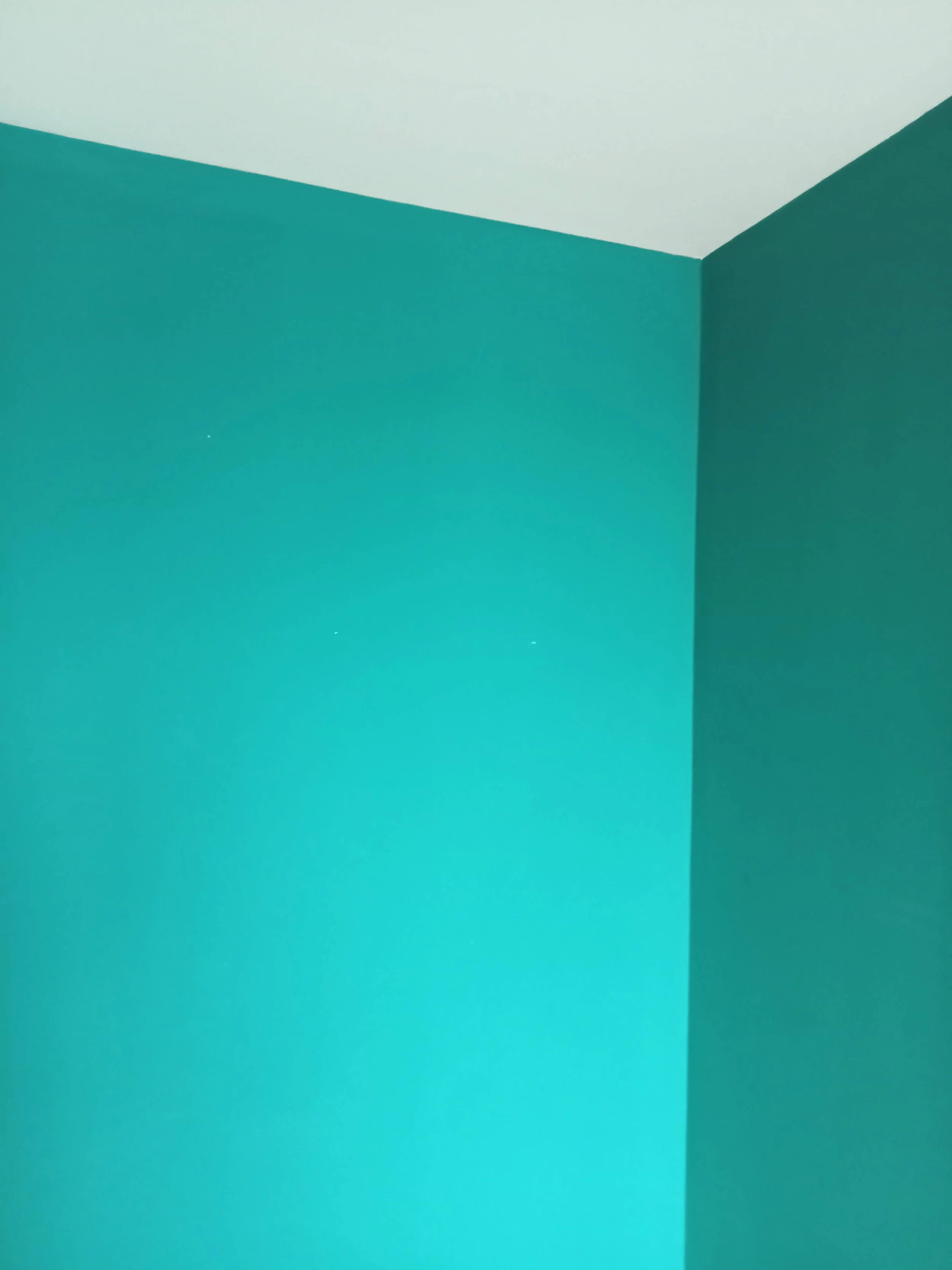 A corner of a room with two walls painted in teal blue and a ceiling painted in off-white.