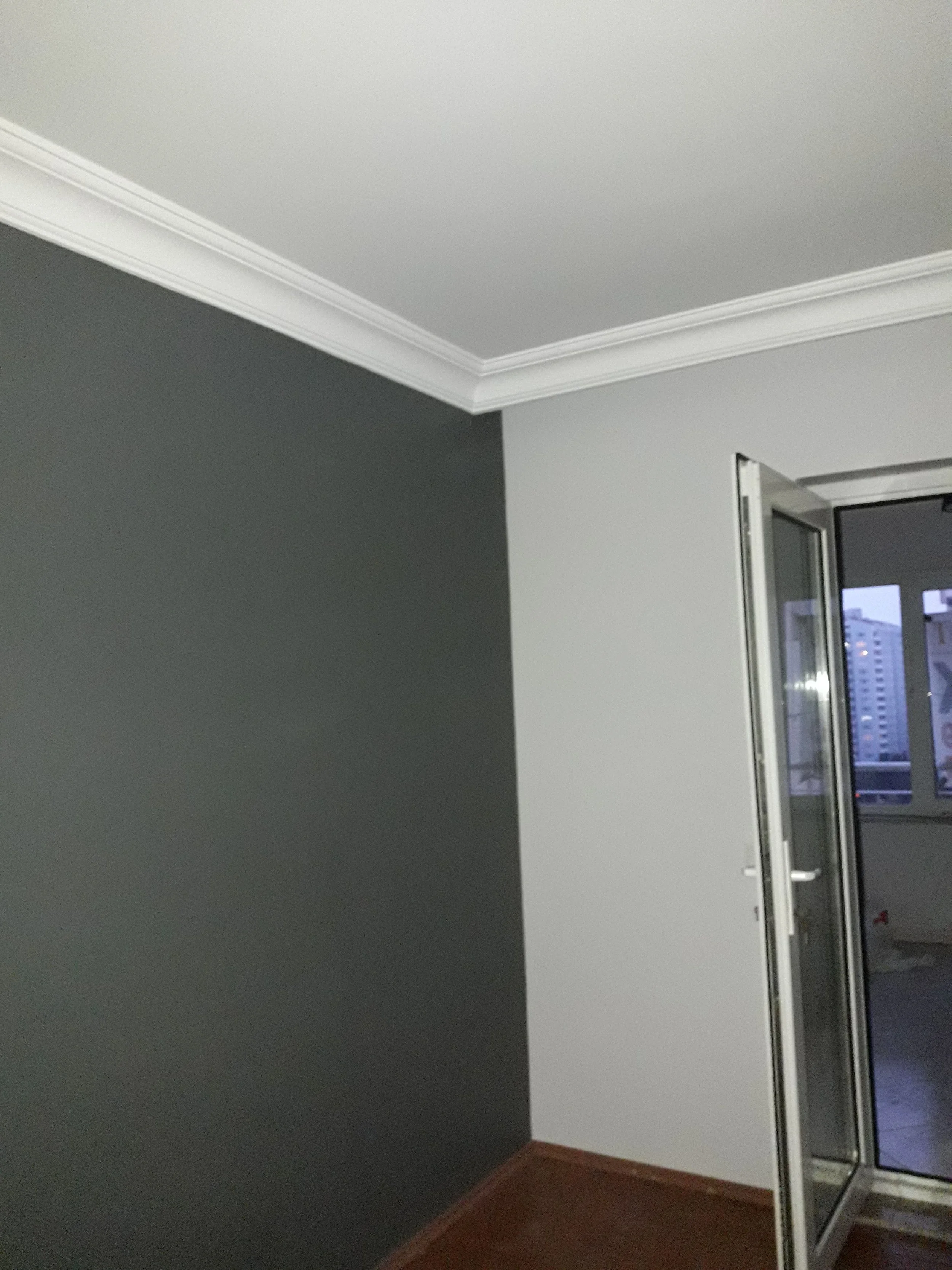Part of an interior room with a gray accent wall, white ceiling with crown molding, and a door with a glass window leading to a balcony or outside area.