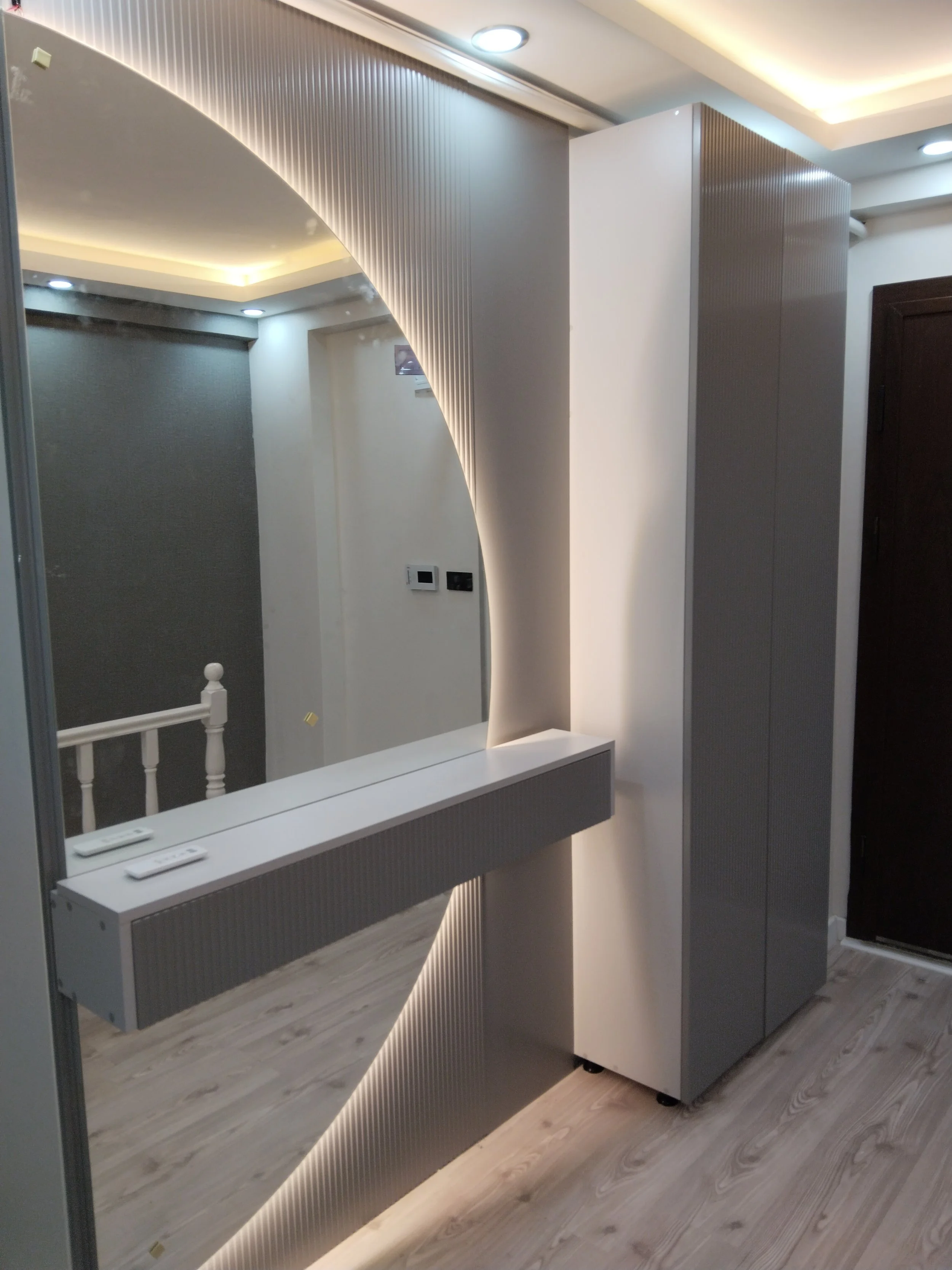Modern interior with a large round mirror, textured wall panels, and a sleek gray cabinet next to a column with LED lighting.