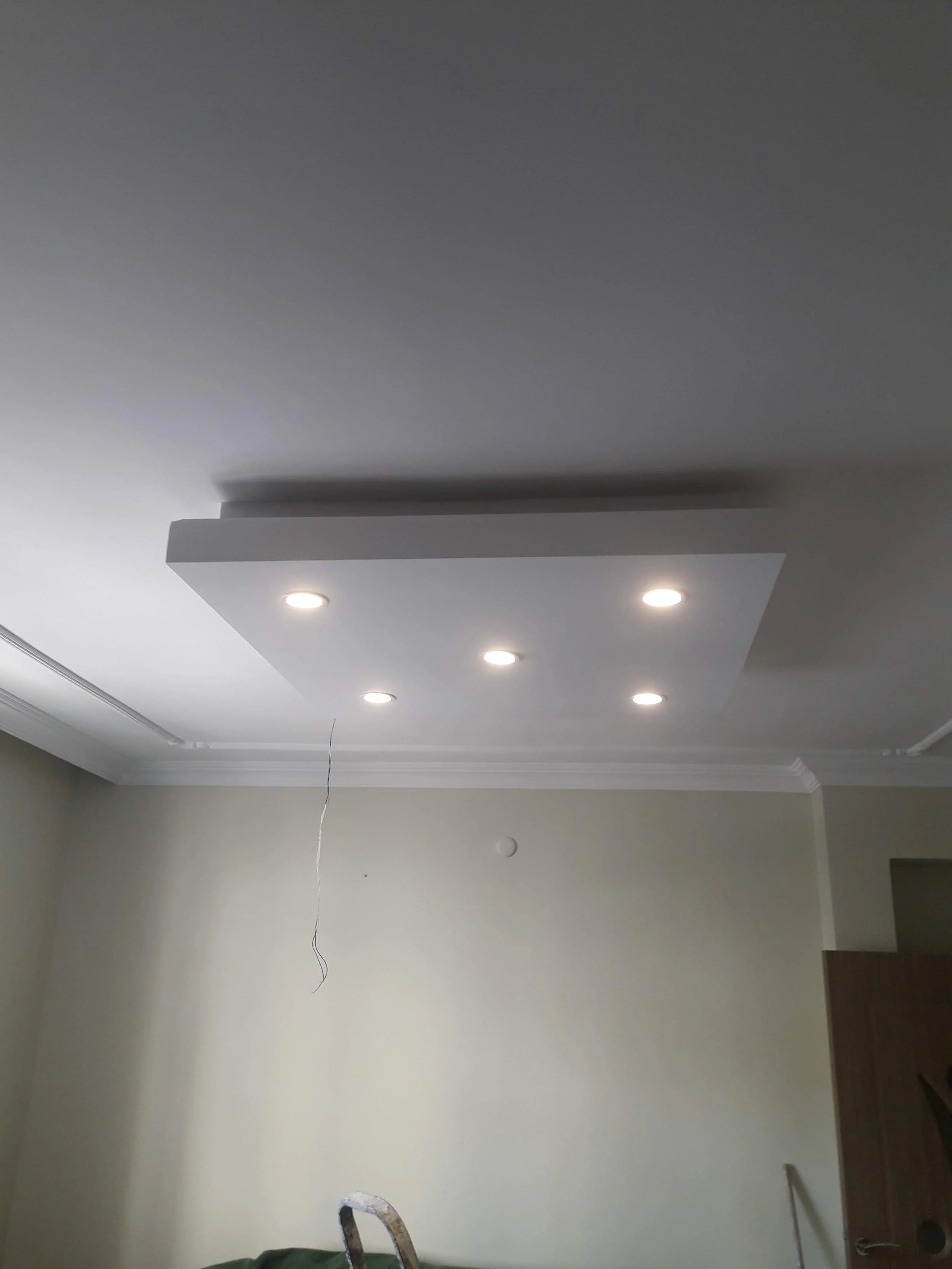 Ceiling with recessed lighting and a false ceiling panel in a living room with beige walls and crown molding.