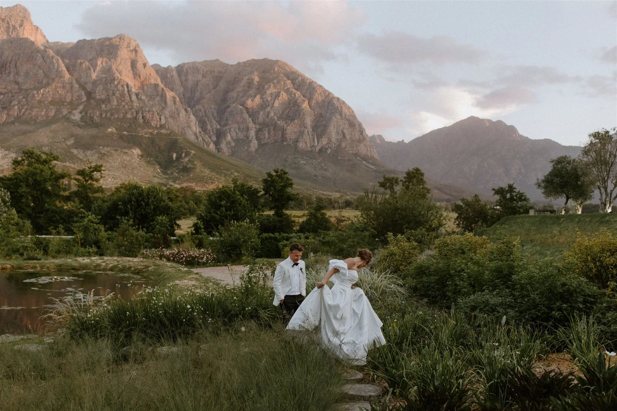 Bride and groom walking through the gardens of Johannesdal 1207 with the surrounding mountains framing the scene.