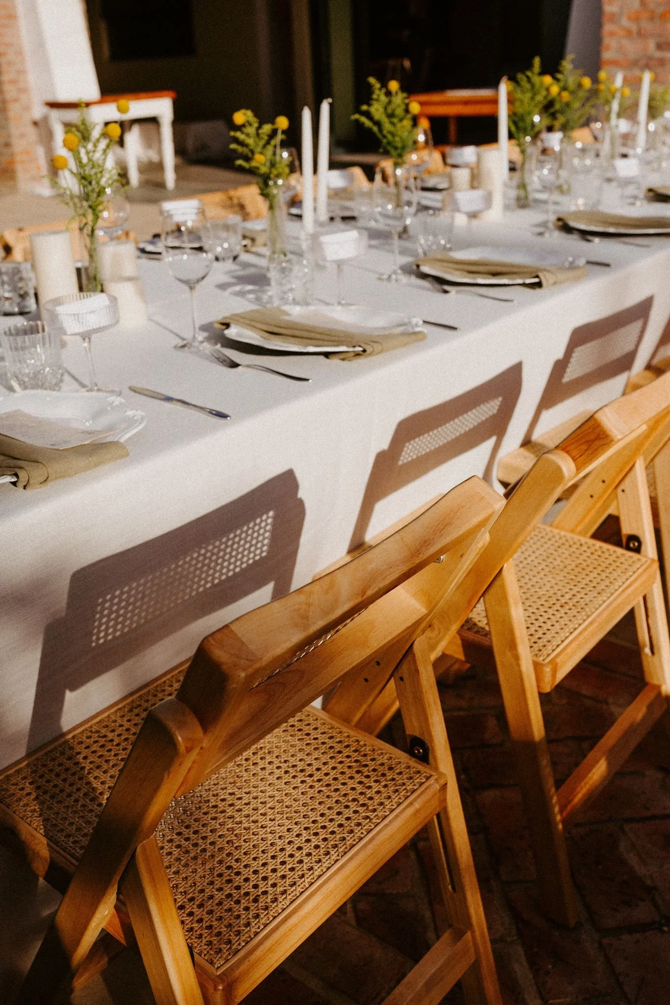Elegant wedding reception table styled with candles, glassware, floral arrangements and wooden chairs.
