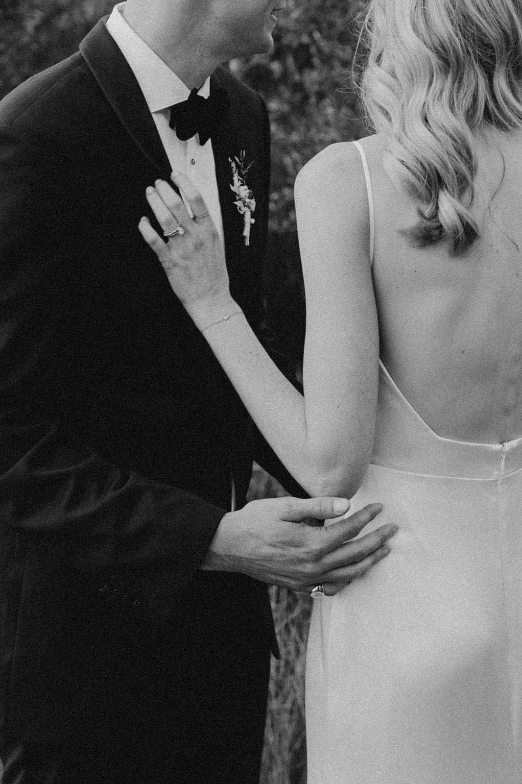 A black and white photo of a man in a tuxedo and a woman in a wedding dress, with the man touching the woman's waist and the woman resting her hand on his chest. Wedding in Cape Town, South Africa captured by wedding photographer Marli Koen.