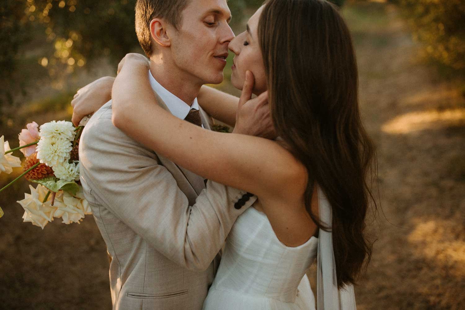 Bride and groom walking through an olive orchard at sunset, with the groom carrying the bride's bouquet at Olijvenkraal Olive & Wine Estate.