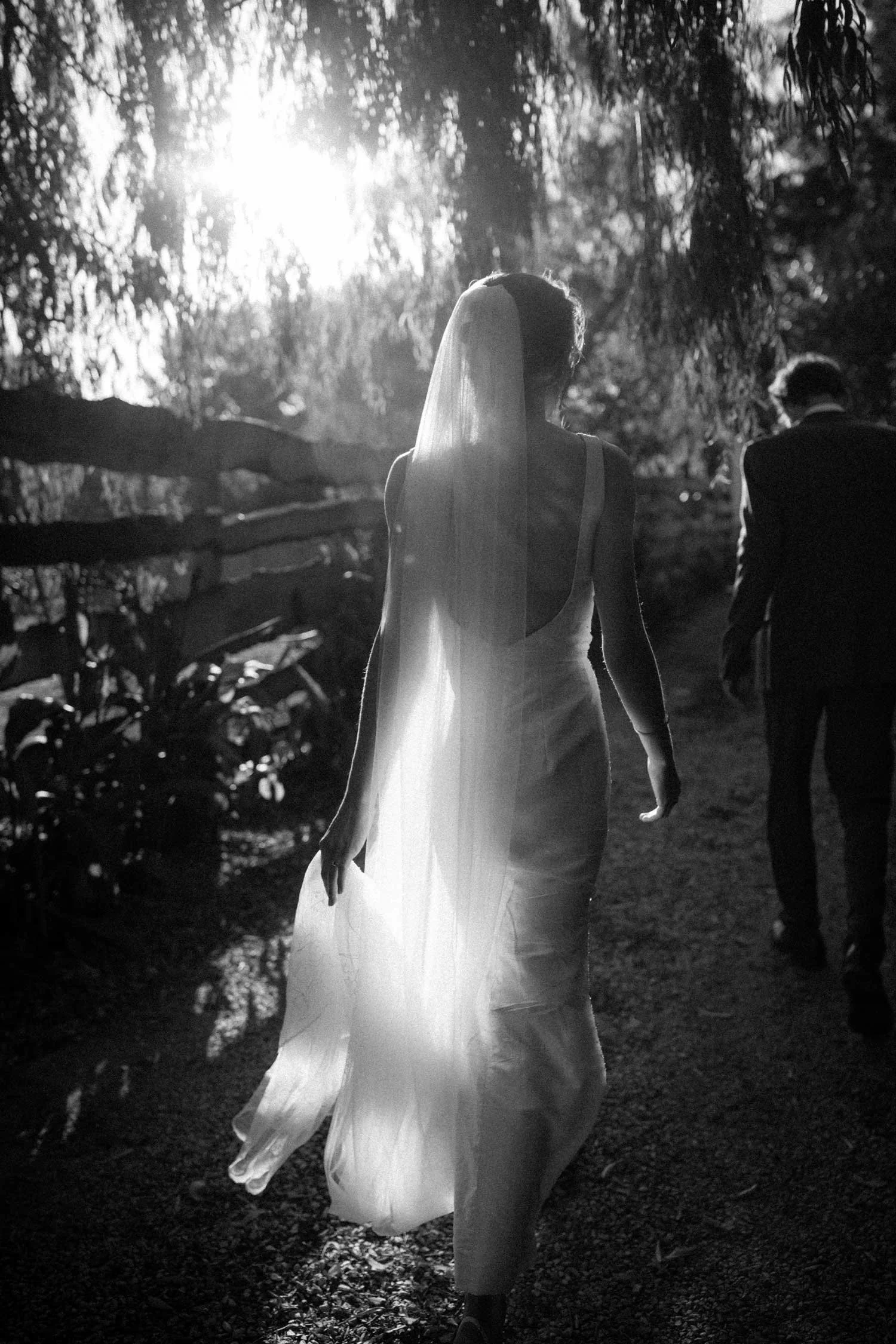 A woman in a wedding dress and veil walking outdoors at sunset, with two men in suits following behind her.