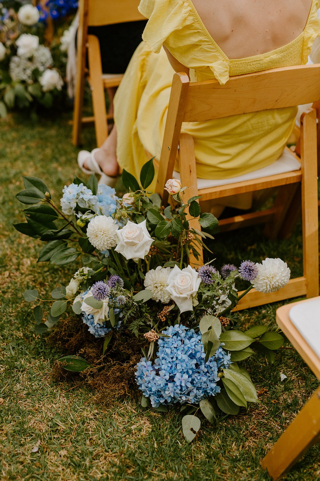 Wedding aisle decorated with blue flowers at Boschendal Olive Press while a guest waits quietly before the ceremony.