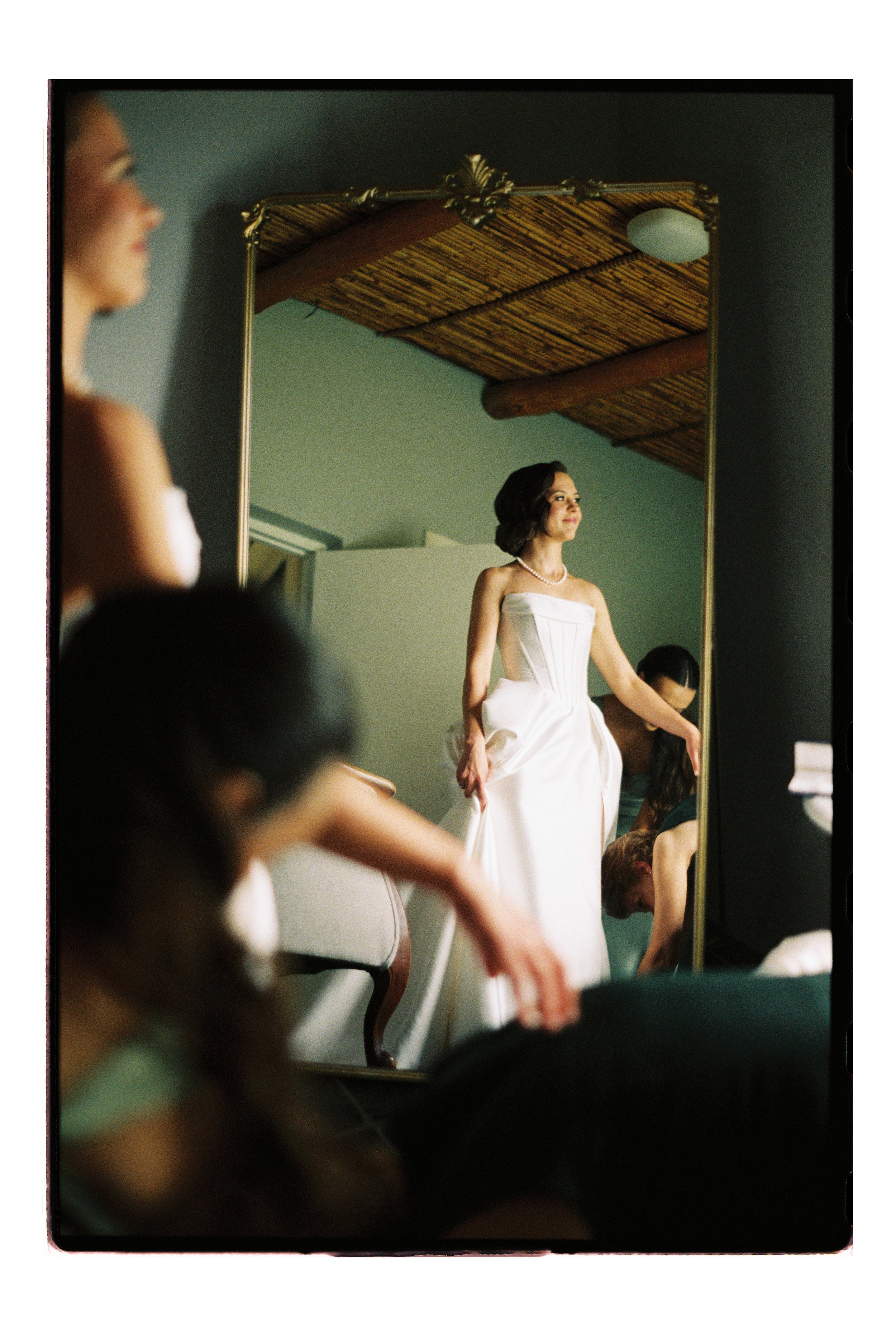 An moment on 35mm film of bride getting dressed in front of mirror at Saronsberg Wine Cellar, Tulbagh