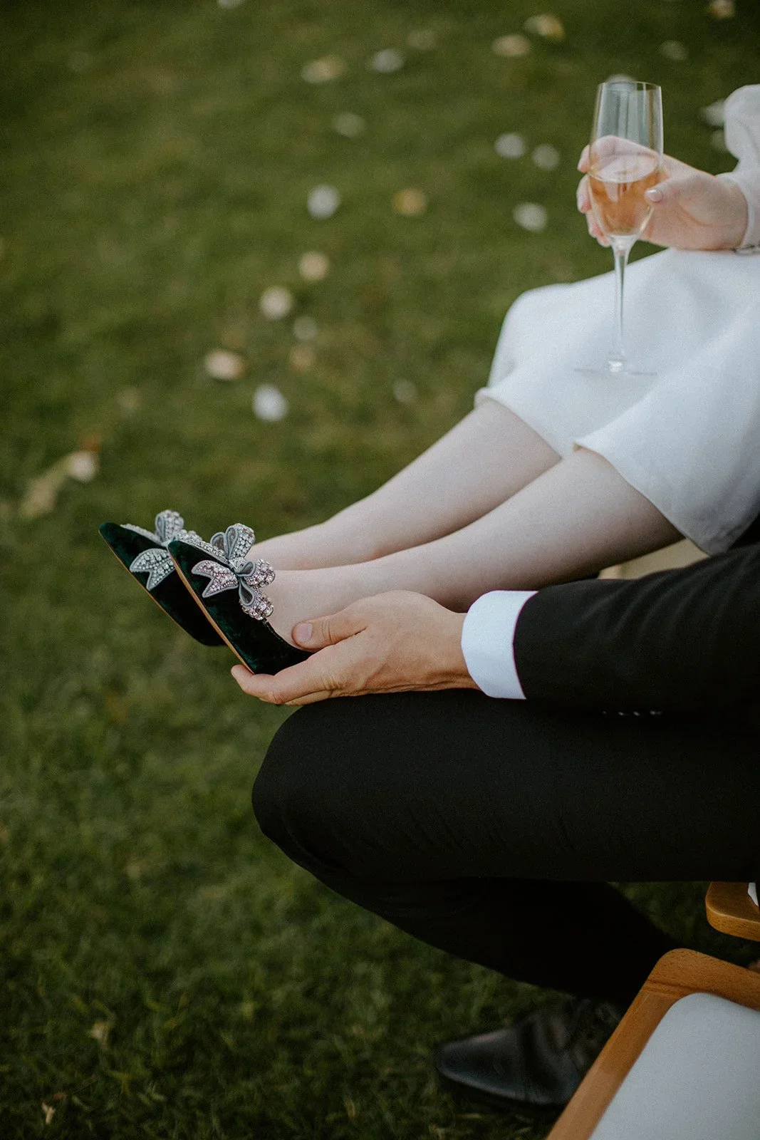 Bride sitting across the groom's lap as they share a glass of champagne and admire her wedding shoes after the ceremony at Boschendal Olive Press.