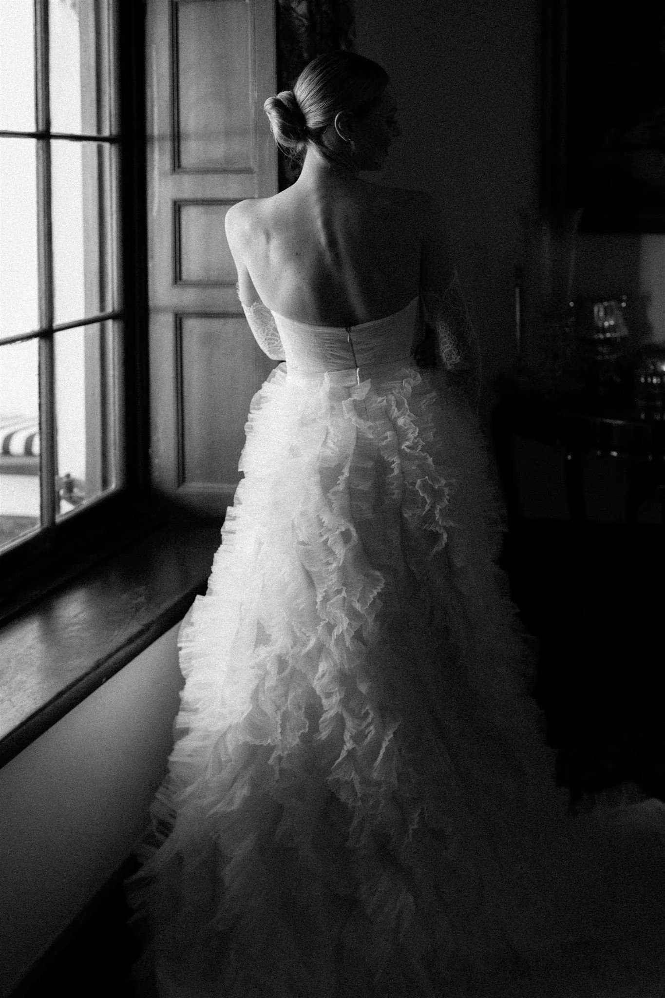 A woman in a wedding dress looking out a window in a black and white photograph. Wedding in Cape Town, South Africa captured by wedding photographer Marli Koen.
