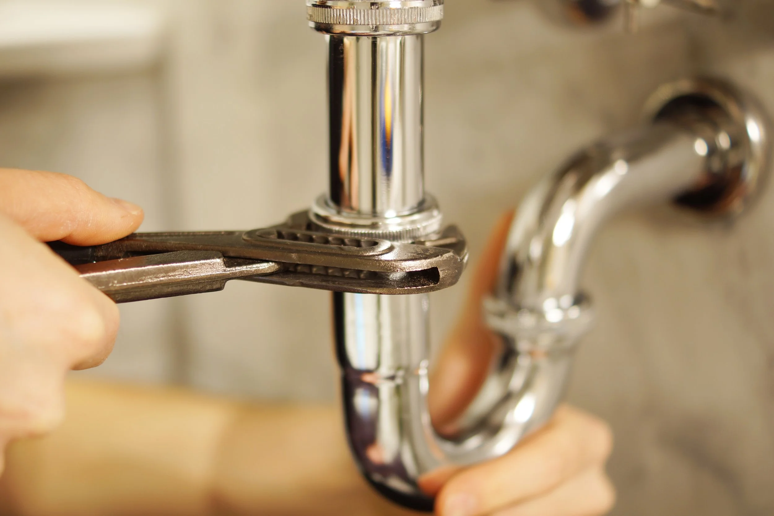 Close-up of a person's hand using a wrench to tighten a plumbing pipe.